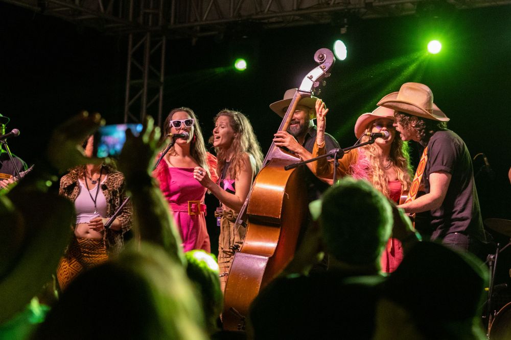 Band performs on outdoor stage with upright bass and festive lighting.