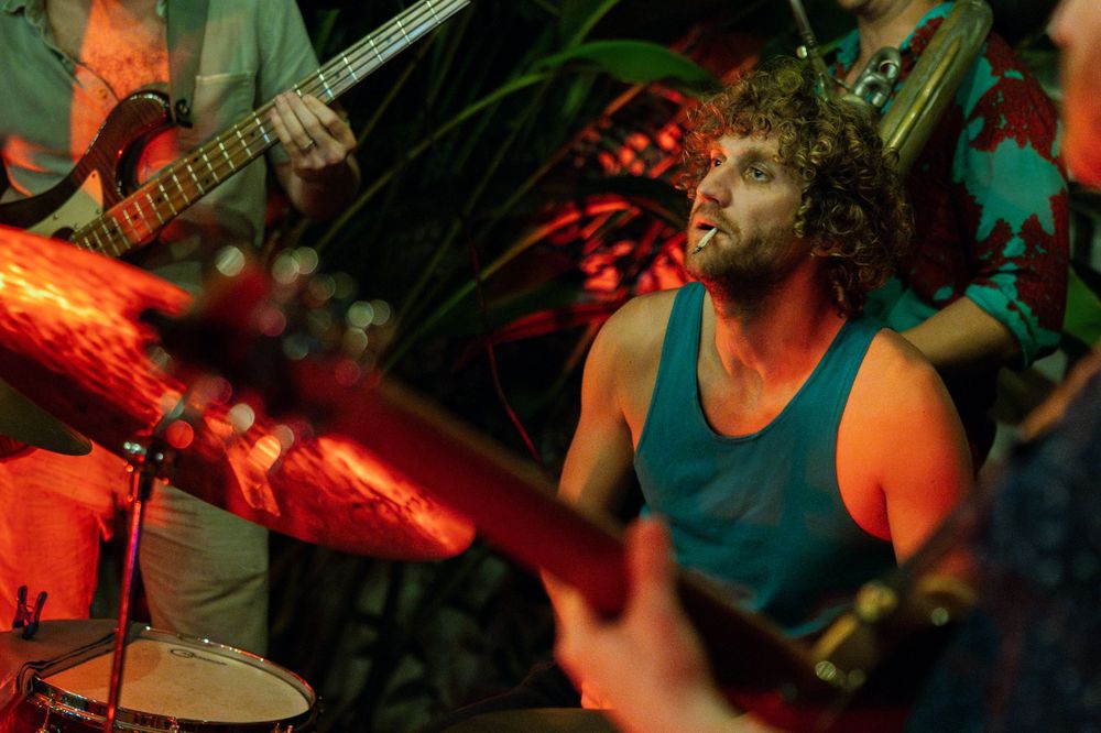 Drummer performs energetically on stage bathed in warm red lighting during a live music show.