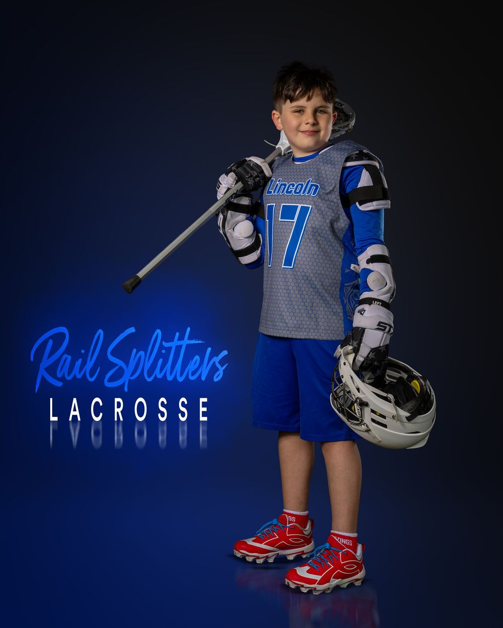 Young lacrosse player in Rail Splitters uniform #17 holding stick and helmet, smiling for team portrait photo.
