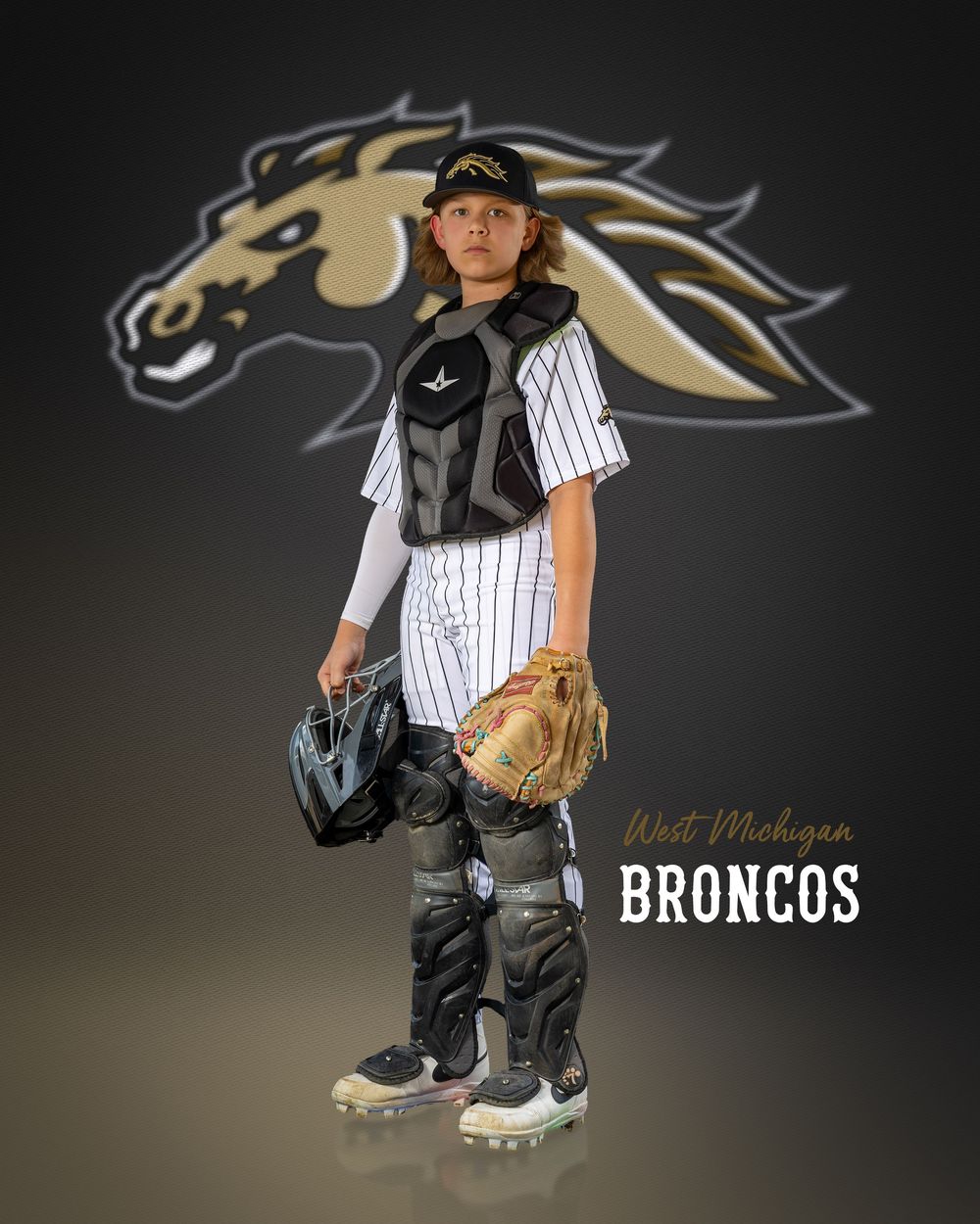 Young baseball catcher in West Michigan Broncos uniform with gear, posing in front of team logo.