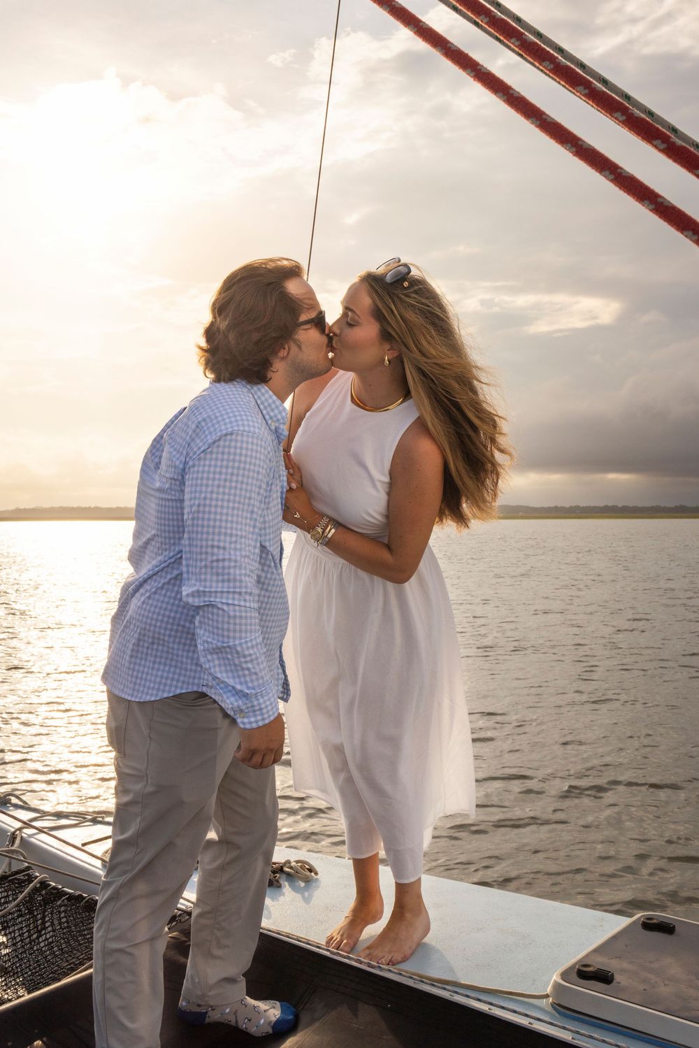 A romantic couple shares a tender kiss at sunset aboard a sailboat on the ocean.