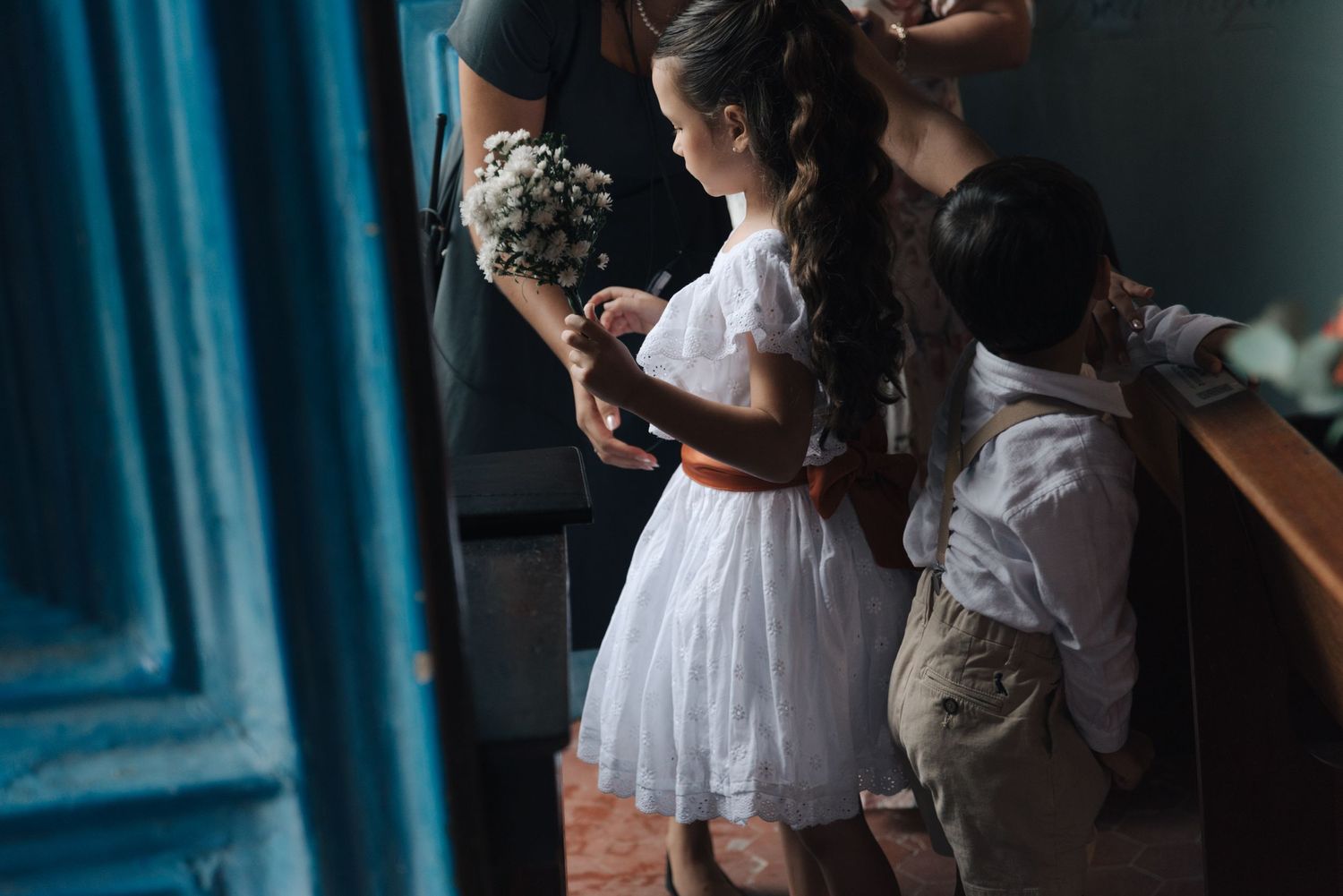Children in formal attire gathering before a wedding ceremony near blue doors.
