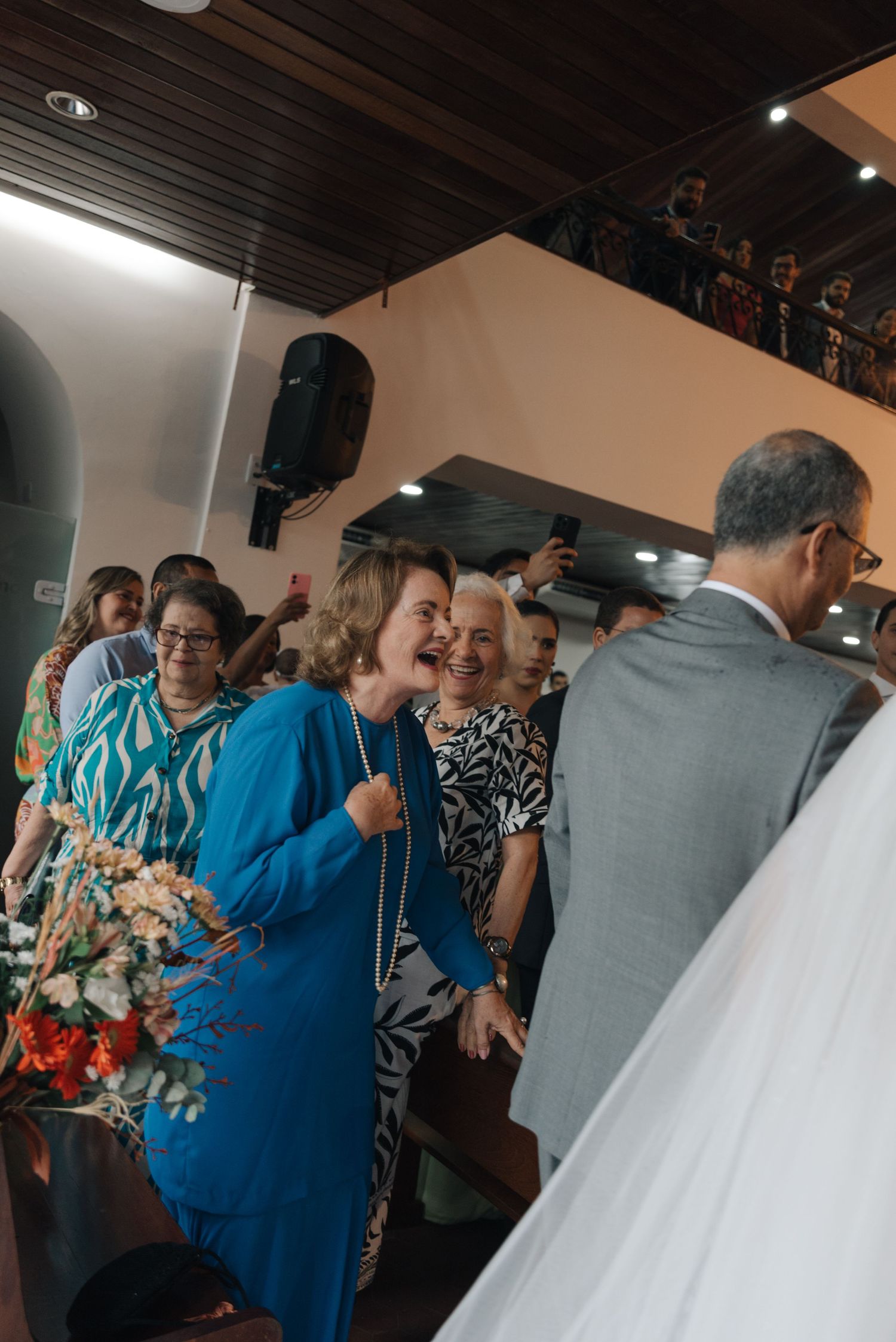 Wedding guests in colorful attire gathering inside a church with wooden ceiling beams.