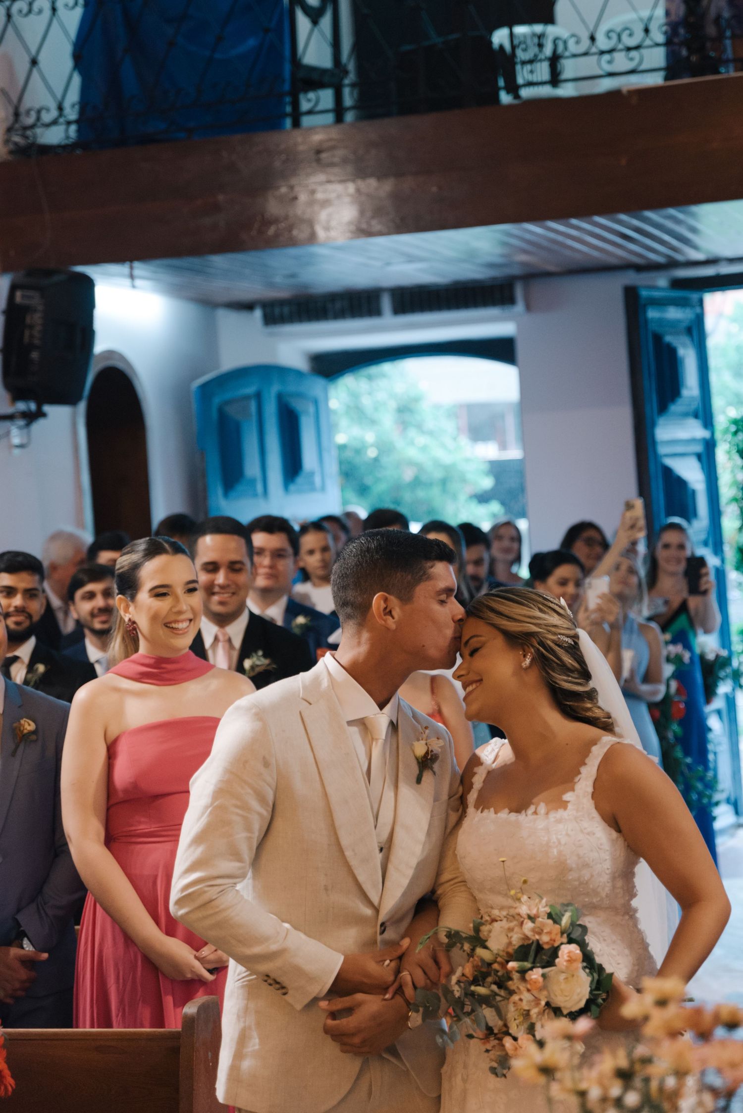 Joyful newlyweds share an intimate moment in church while wedding guests look on.