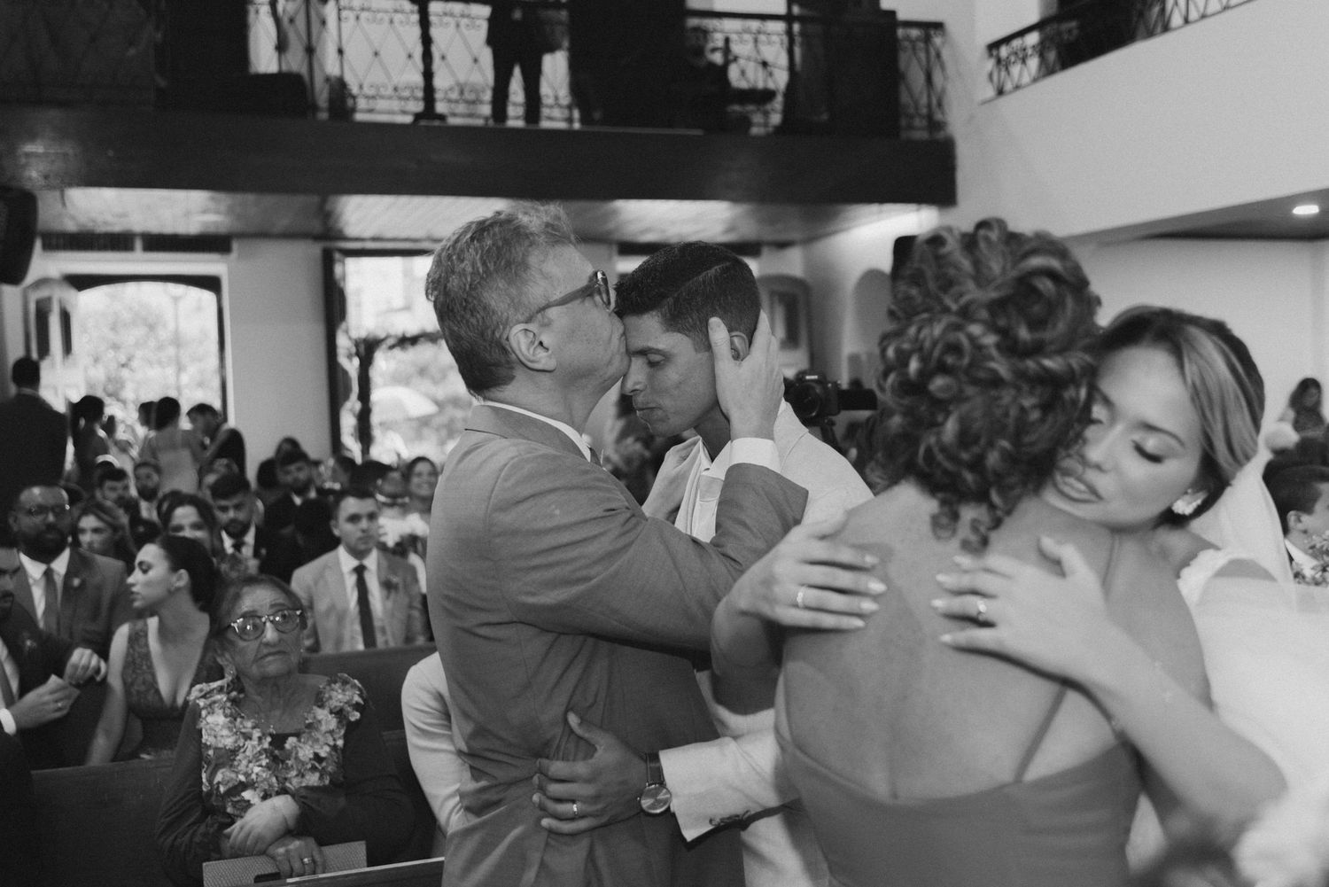 Black and white photo of multiple embraces during an emotional wedding moment.