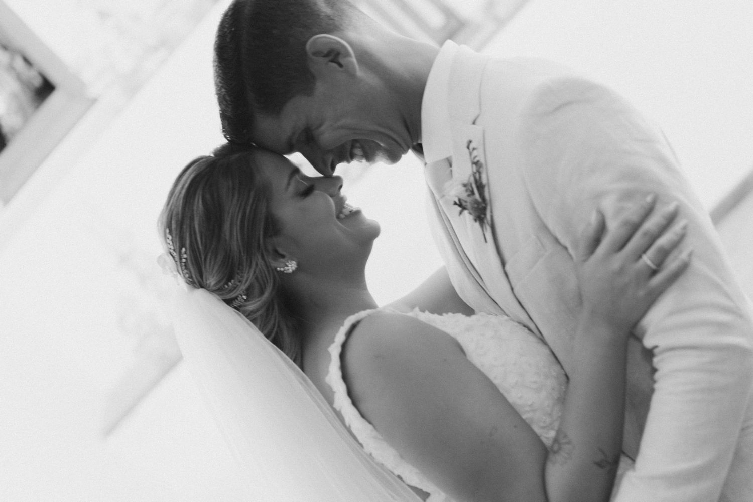 A black and white portrait of a bride and groom sharing an intimate moment in their wedding attire.