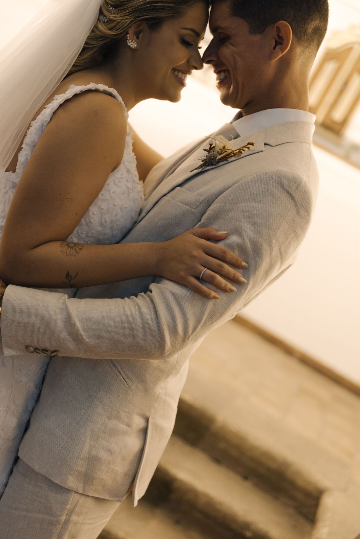 A joyful bride and groom share a close embrace while wearing light colored wedding attire.