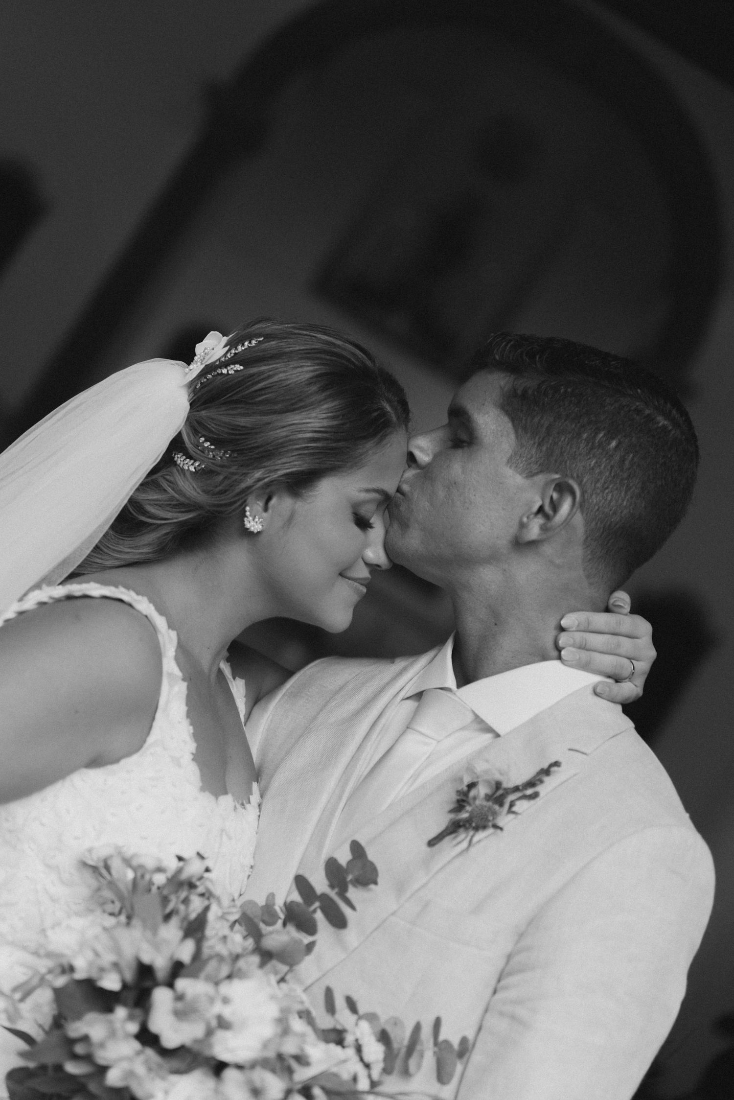 A black and white portrait shows a bride and groom sharing a romantic moment with flowers.