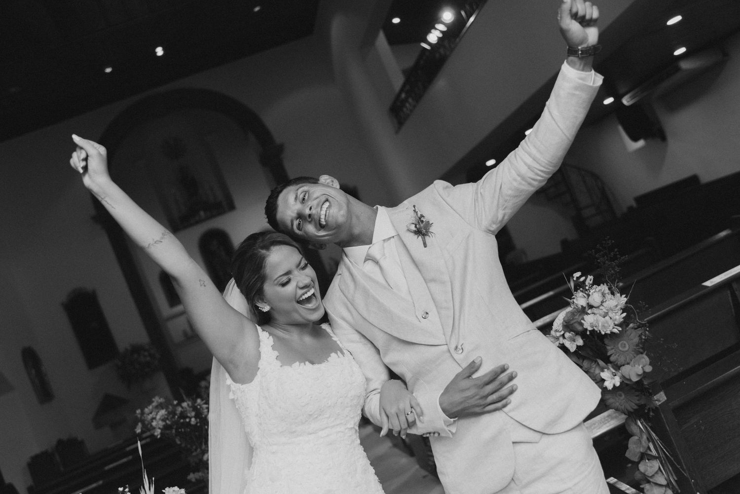 Energetic black and white photo of newlyweds celebrating with raised arms in a church setting.