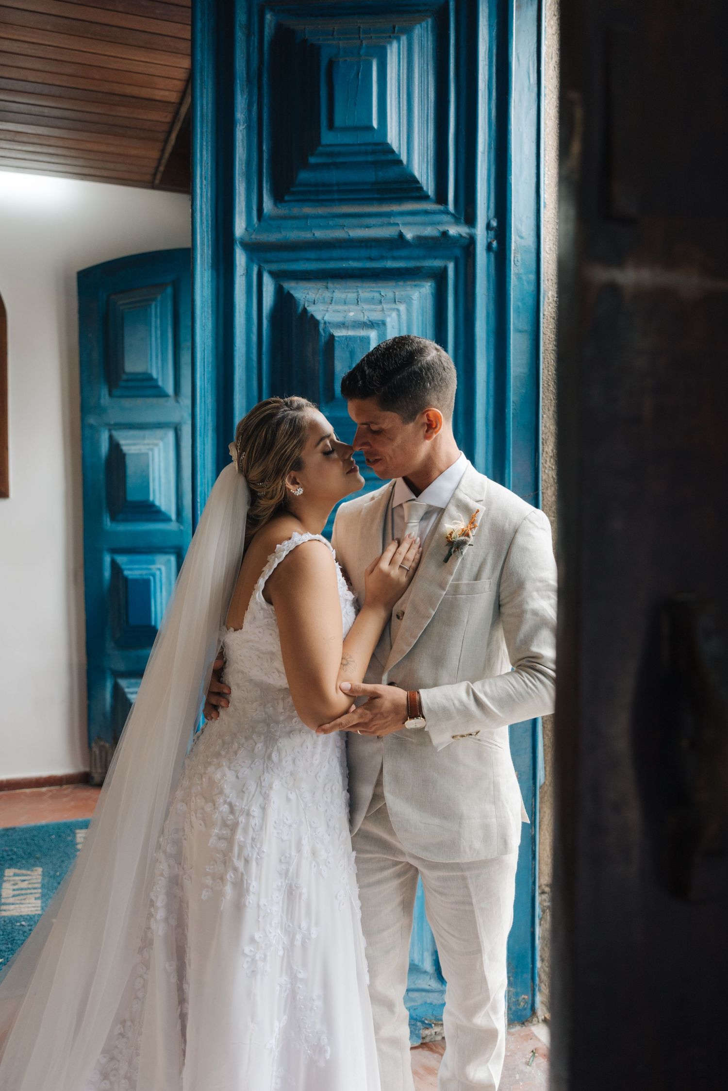 Elegant wedding portrait featuring the couple in white attire against ornate blue church doors.