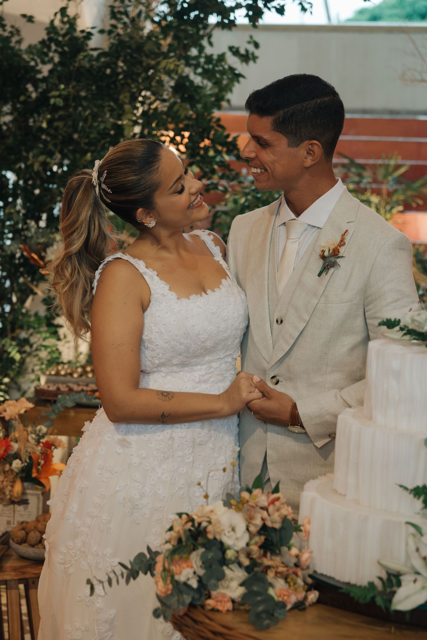 A couple in wedding attire share a joyful moment beside their wedding cake.