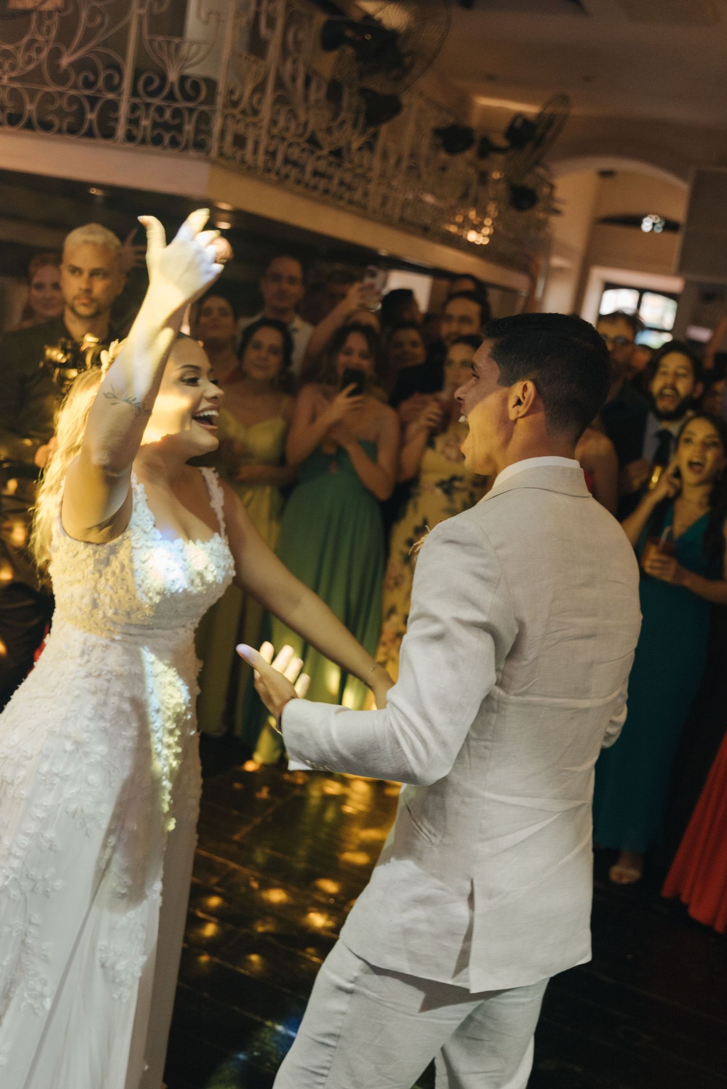 Wedding couple dancing energetically during their first dance while guests cheer in the background.