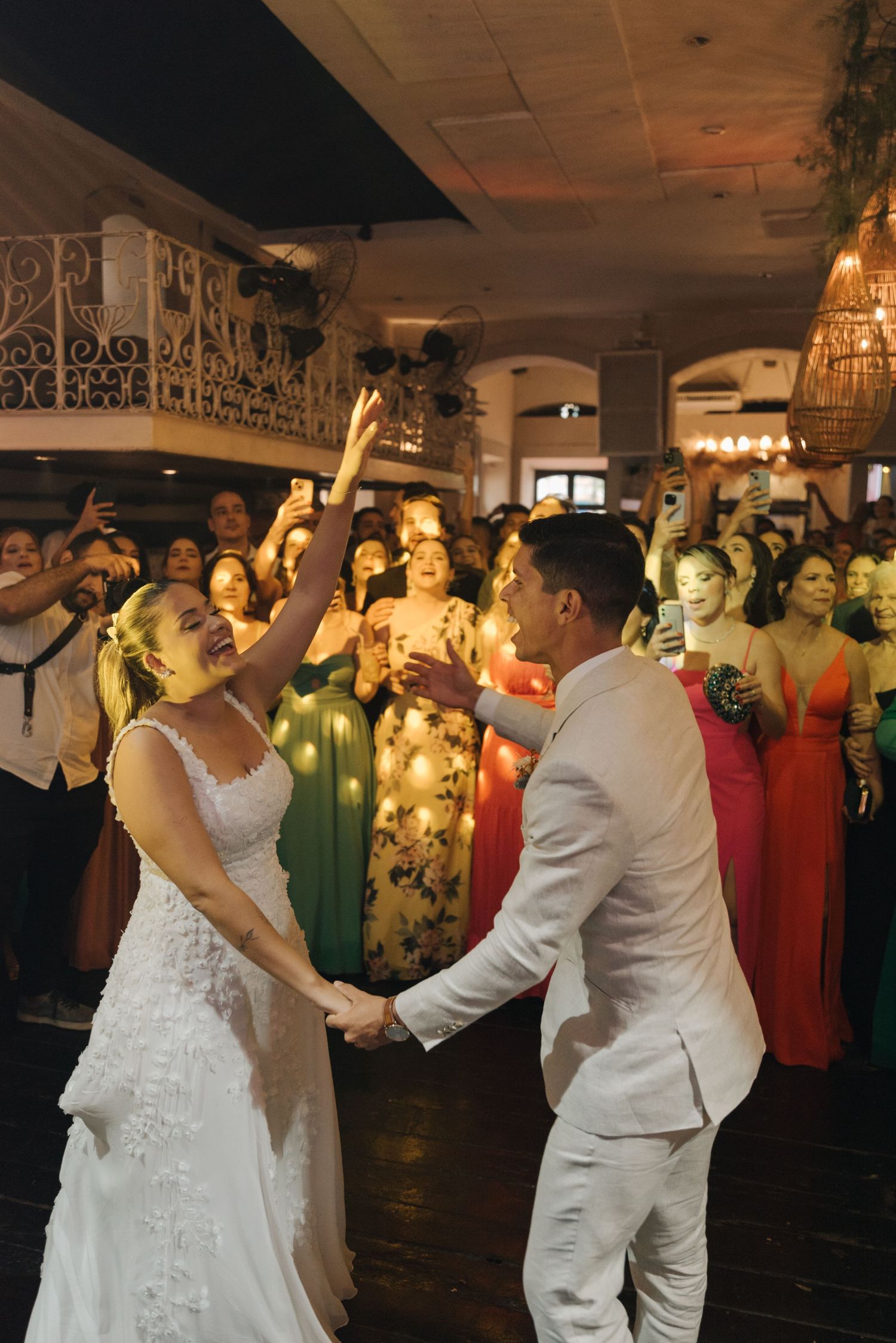 A wedding couple performs their first dance surrounded by celebrating guests in a beautifully lit venue.