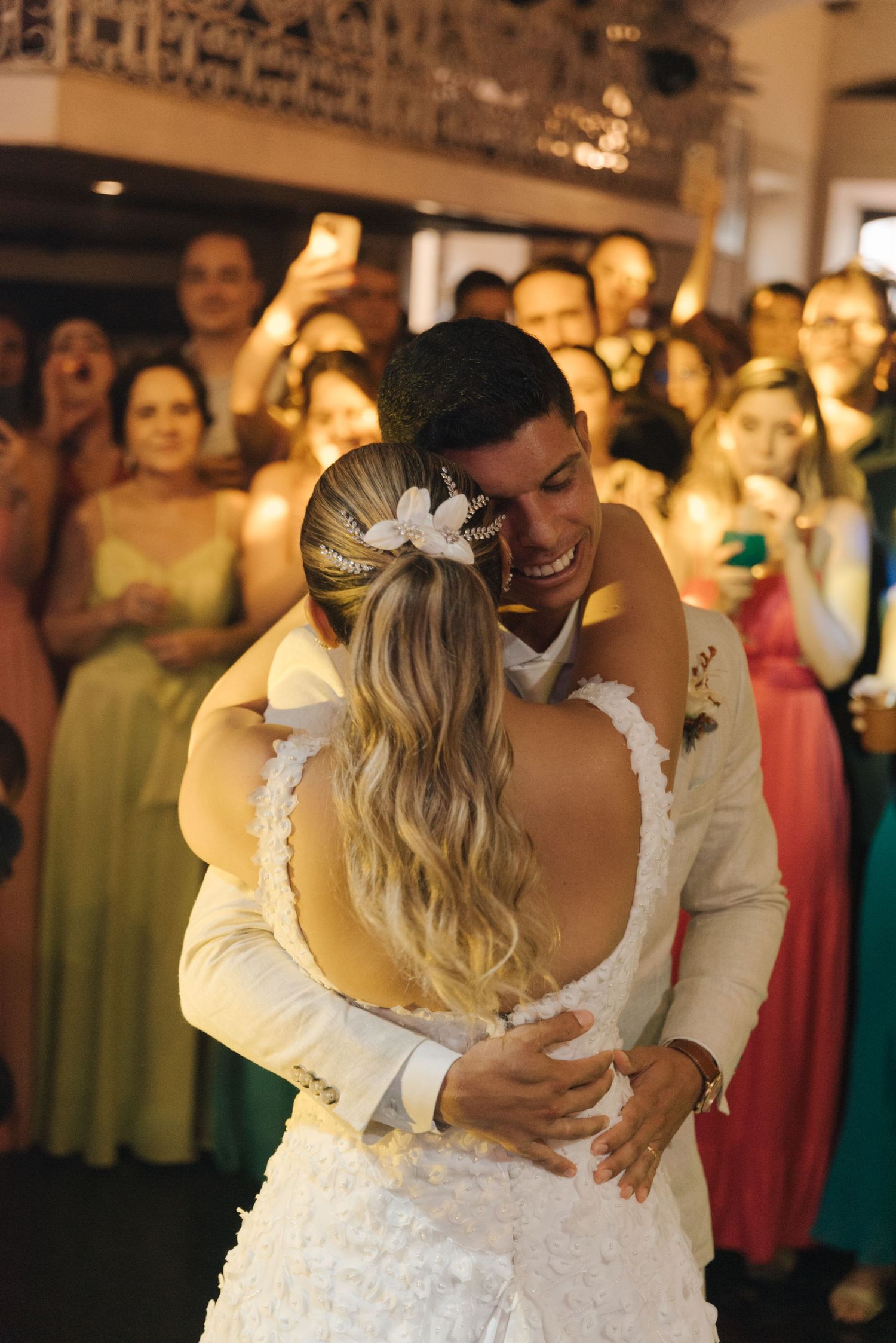 Newlyweds share an intimate moment during their wedding dance while guests watch and take photos.