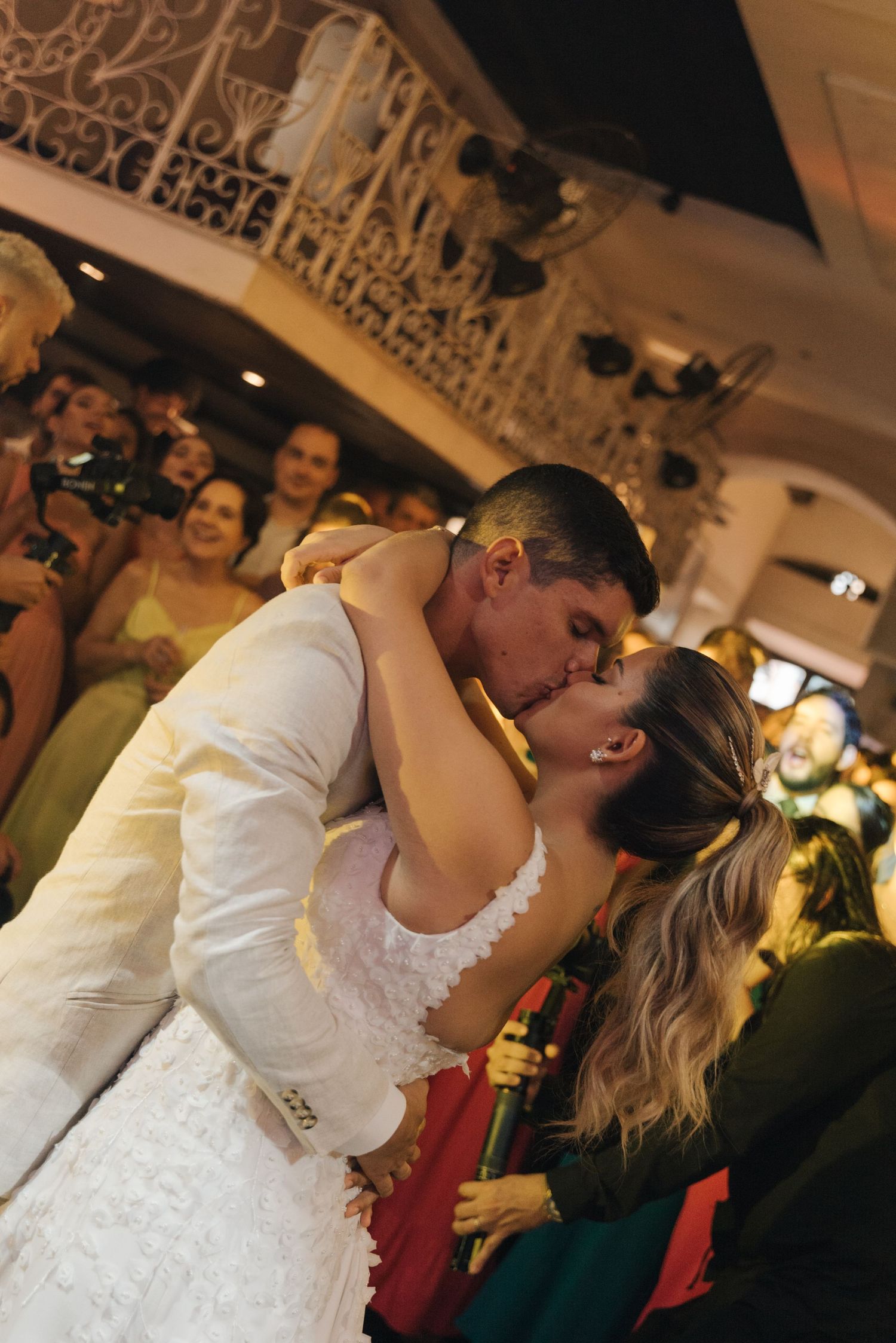 A romantic dip kiss between newlyweds during their wedding dance with guests watching in background.