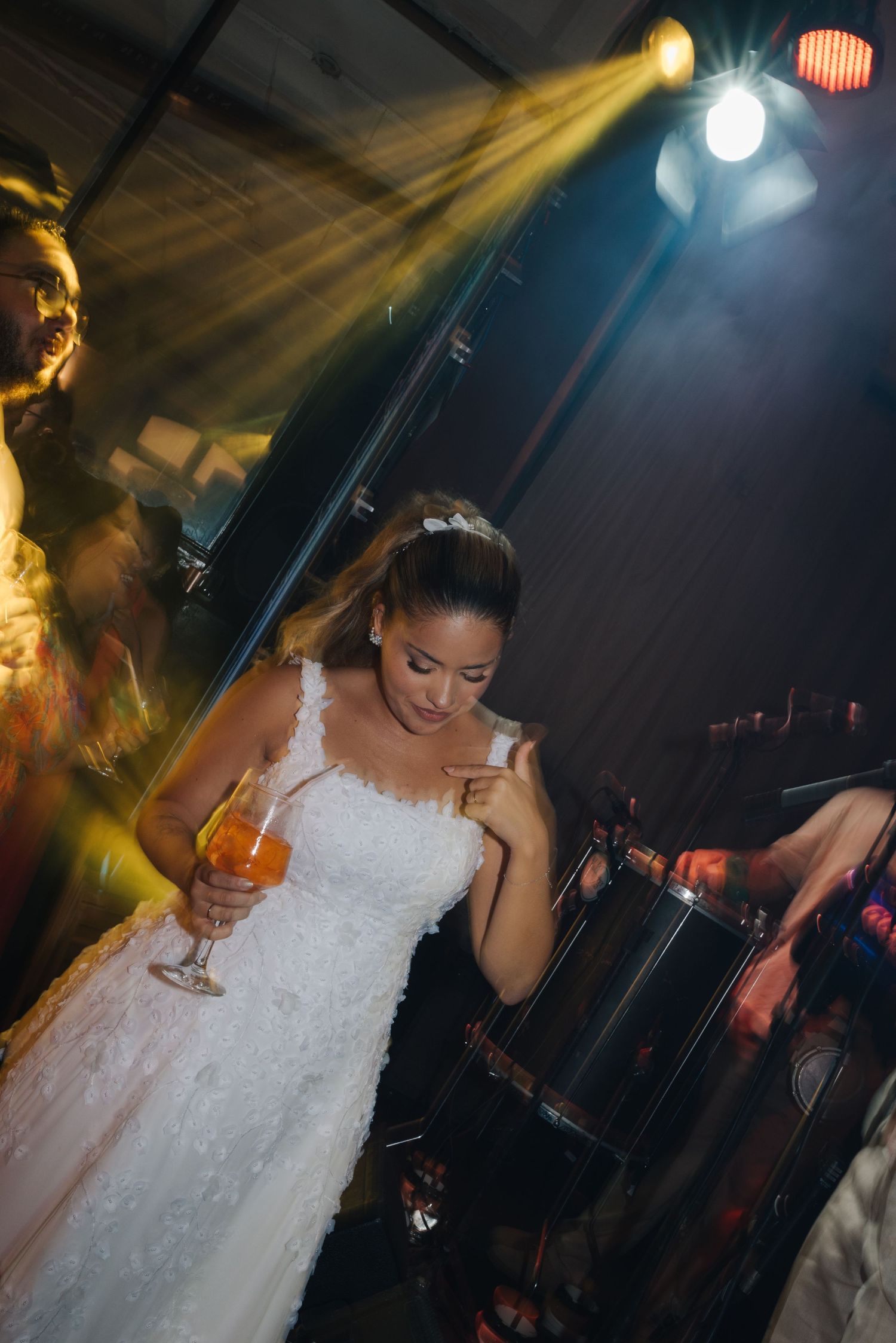 Bride holding a cocktail while dancing under dramatic venue lighting at wedding reception.