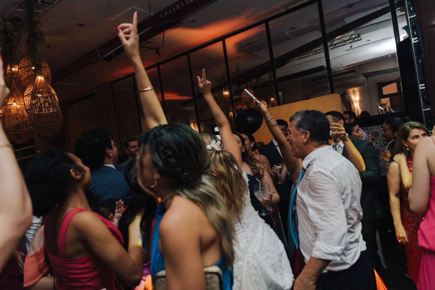 Wedding party guests dancing with hands in the air under orange ambient lighting.