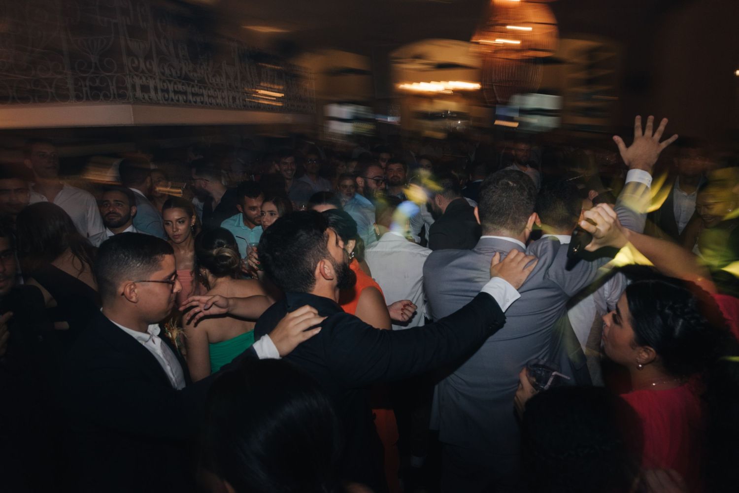 Energetic crowd dancing and raising their hands on a dimly lit dance floor at a wedding reception.