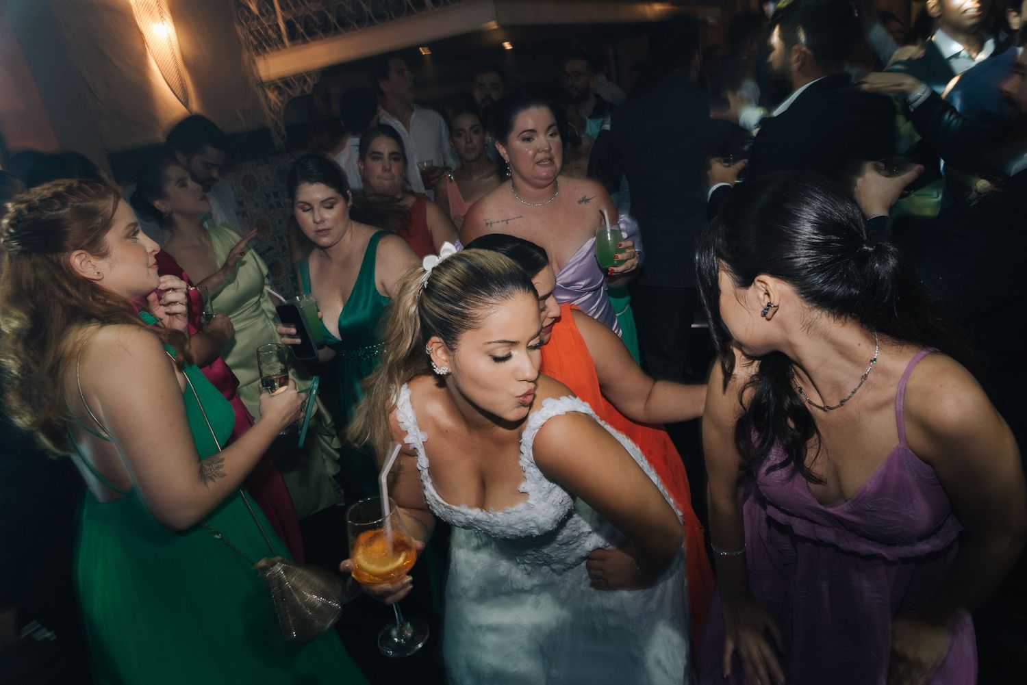 Wedding guests in colorful dresses dancing and celebrating on the dance floor.