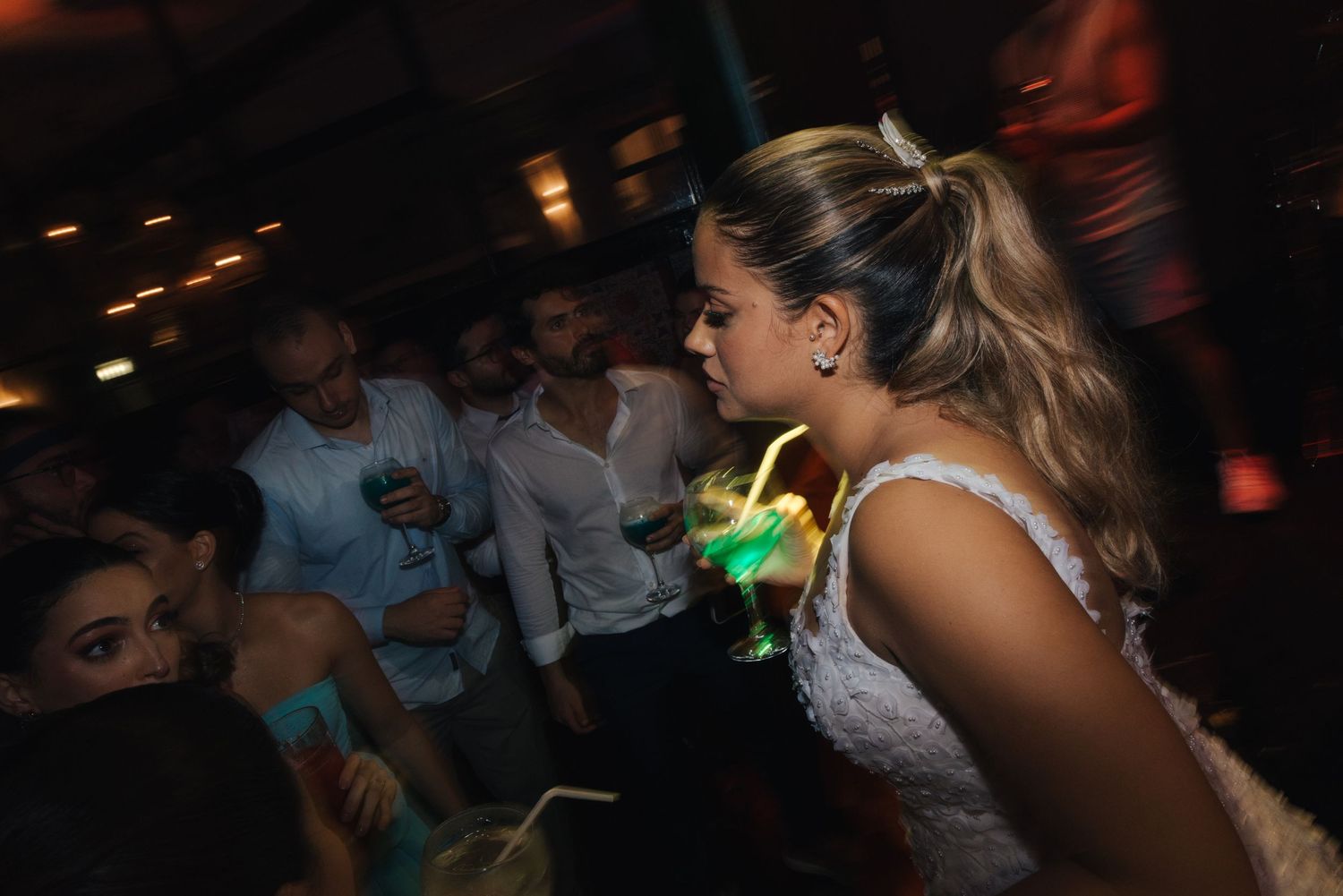 A bride enjoying her reception party while holding a glowing green drink.