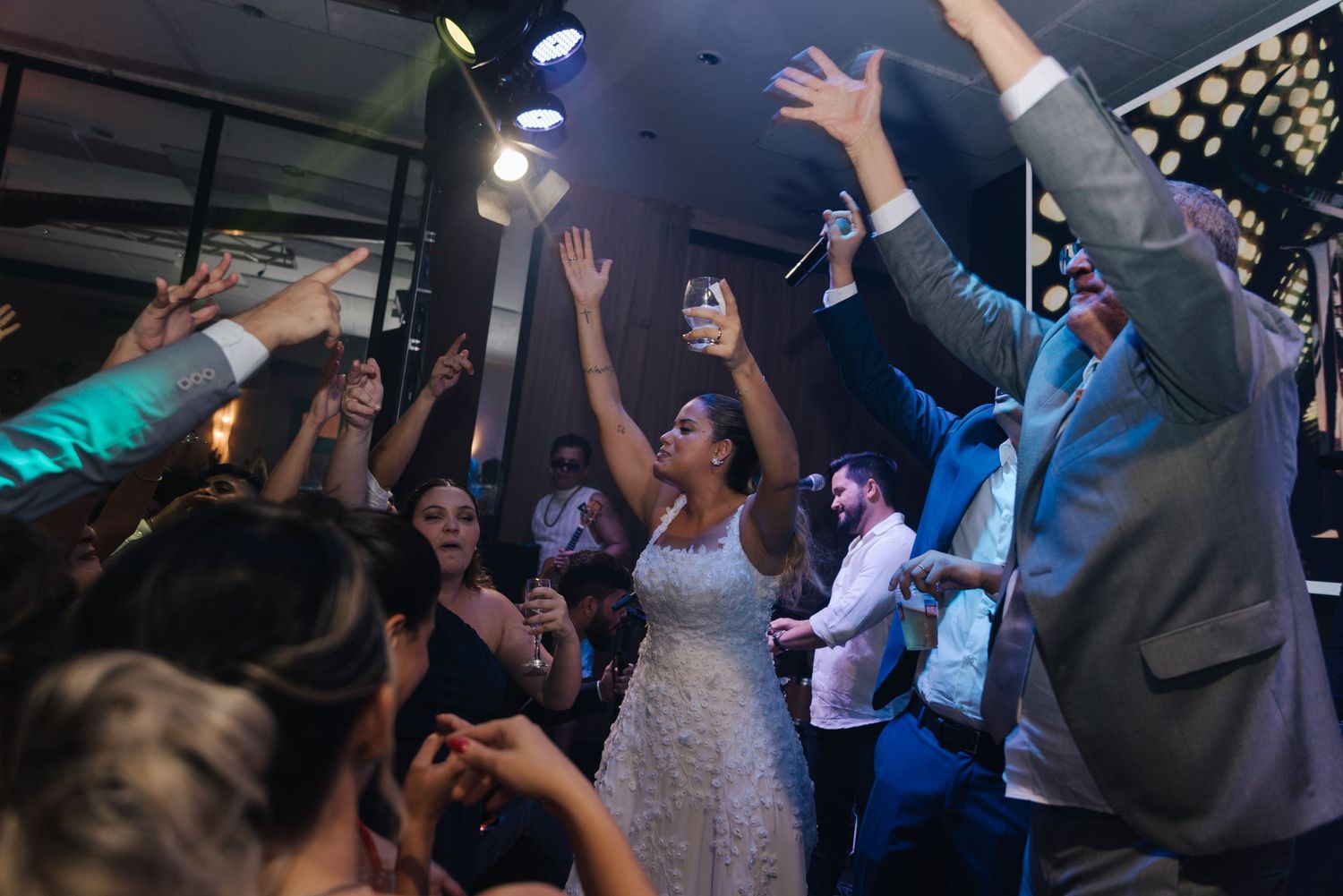 Wedding guests and the bride dance with hands in the air during reception celebrations.