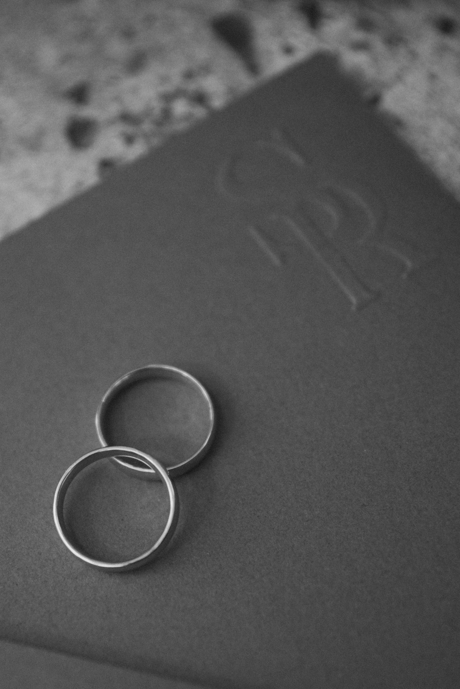 Two wedding rings arranged on a dark textured surface in black and white.