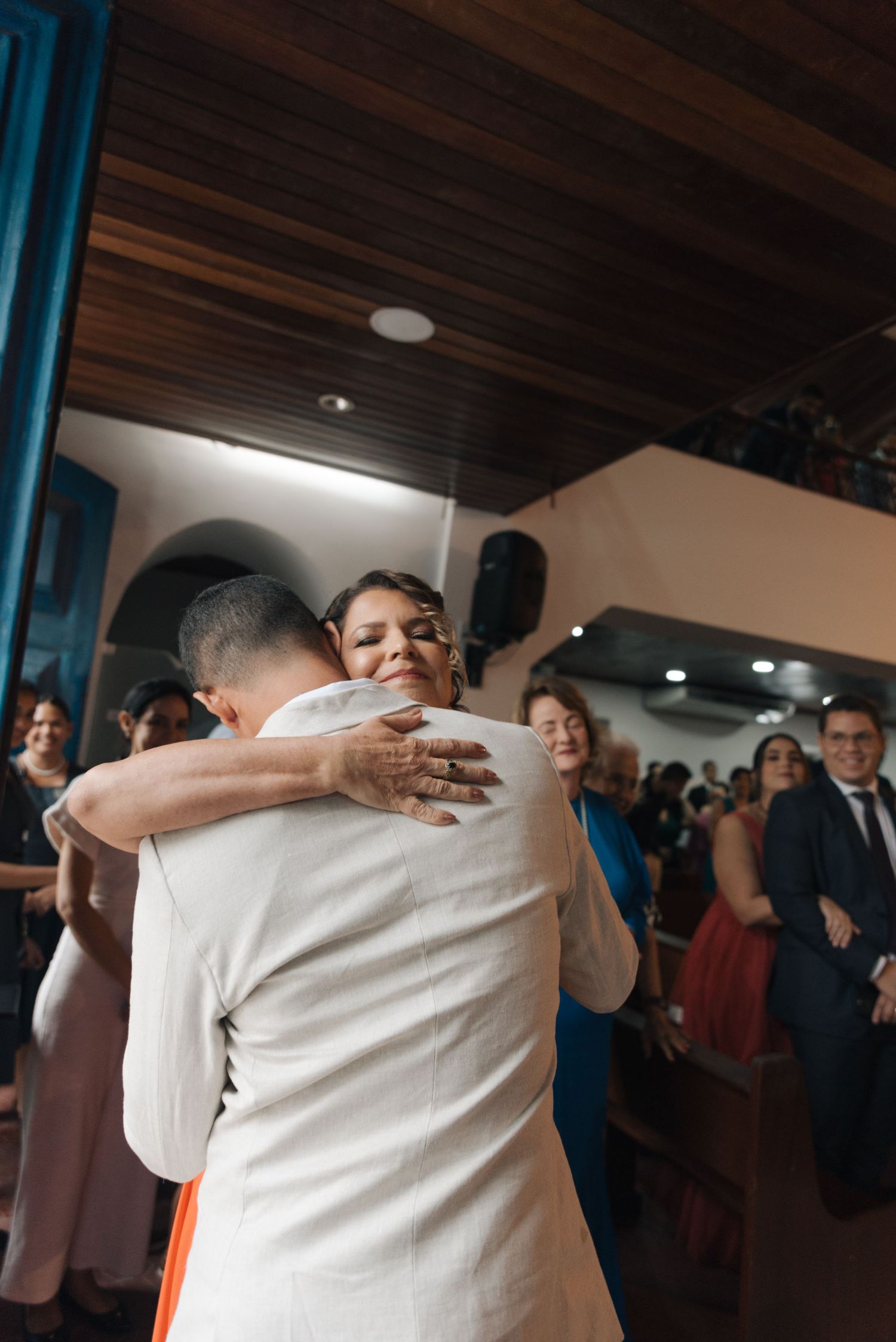 Emotional embrace during wedding celebration with guests in background.