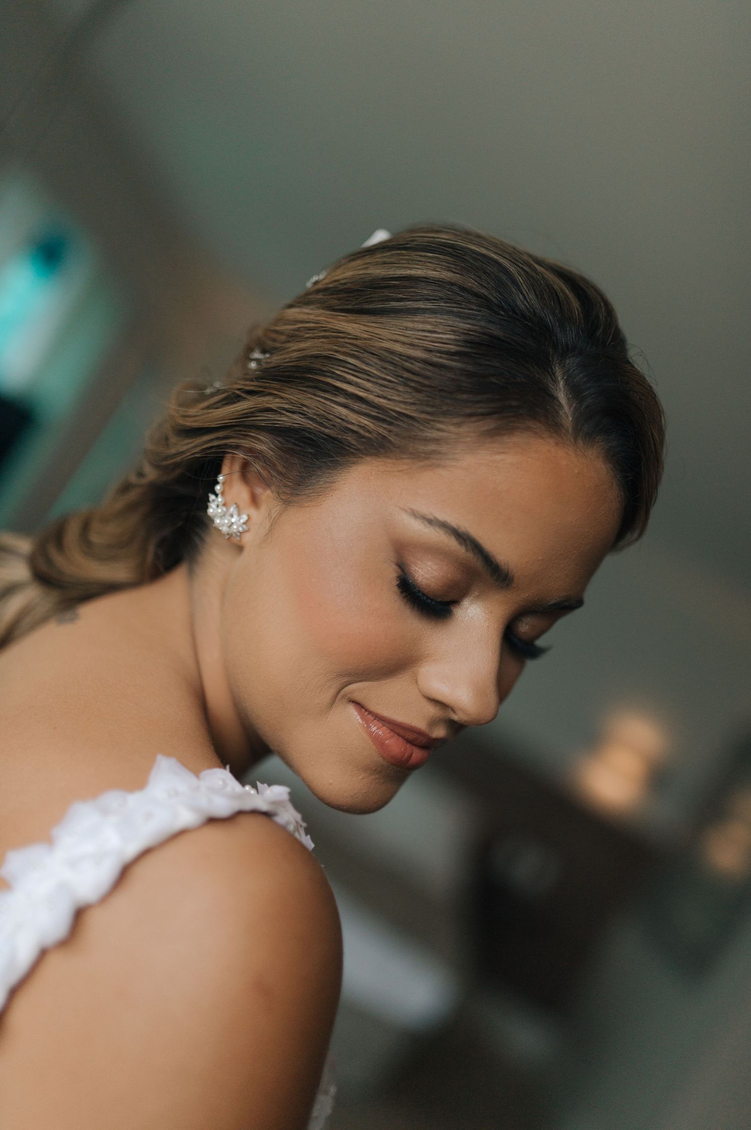 A close-up shot of a bride with delicate earrings and natural makeup looking down.