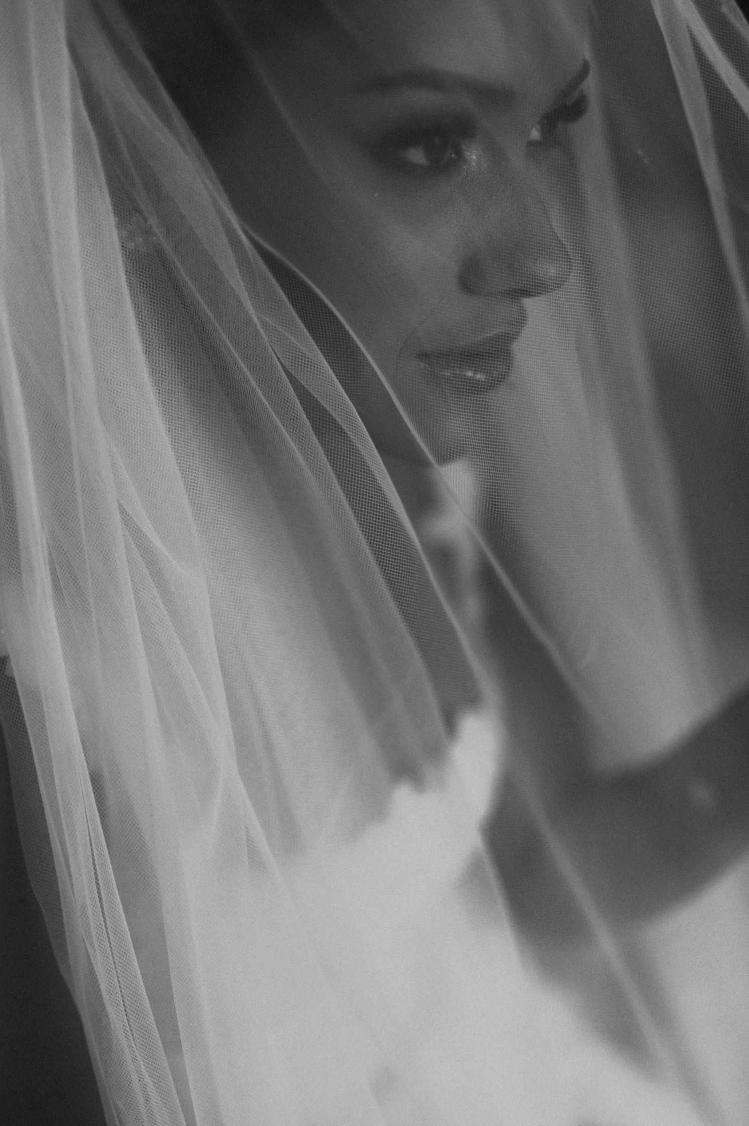Artistic black and white close-up of a bride behind a delicate veil showing side profile.
