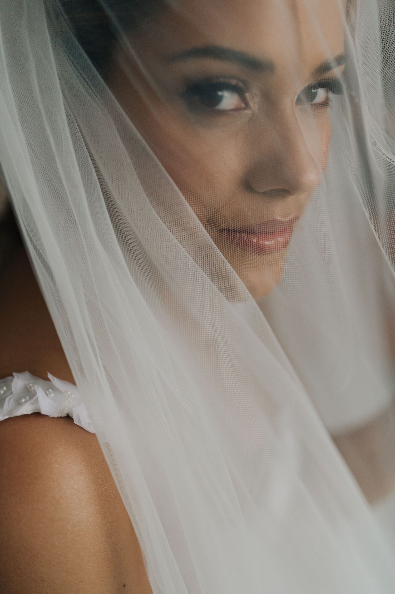 Close-up portrait of bride wearing sheer veil with soft natural makeup and serene expression.