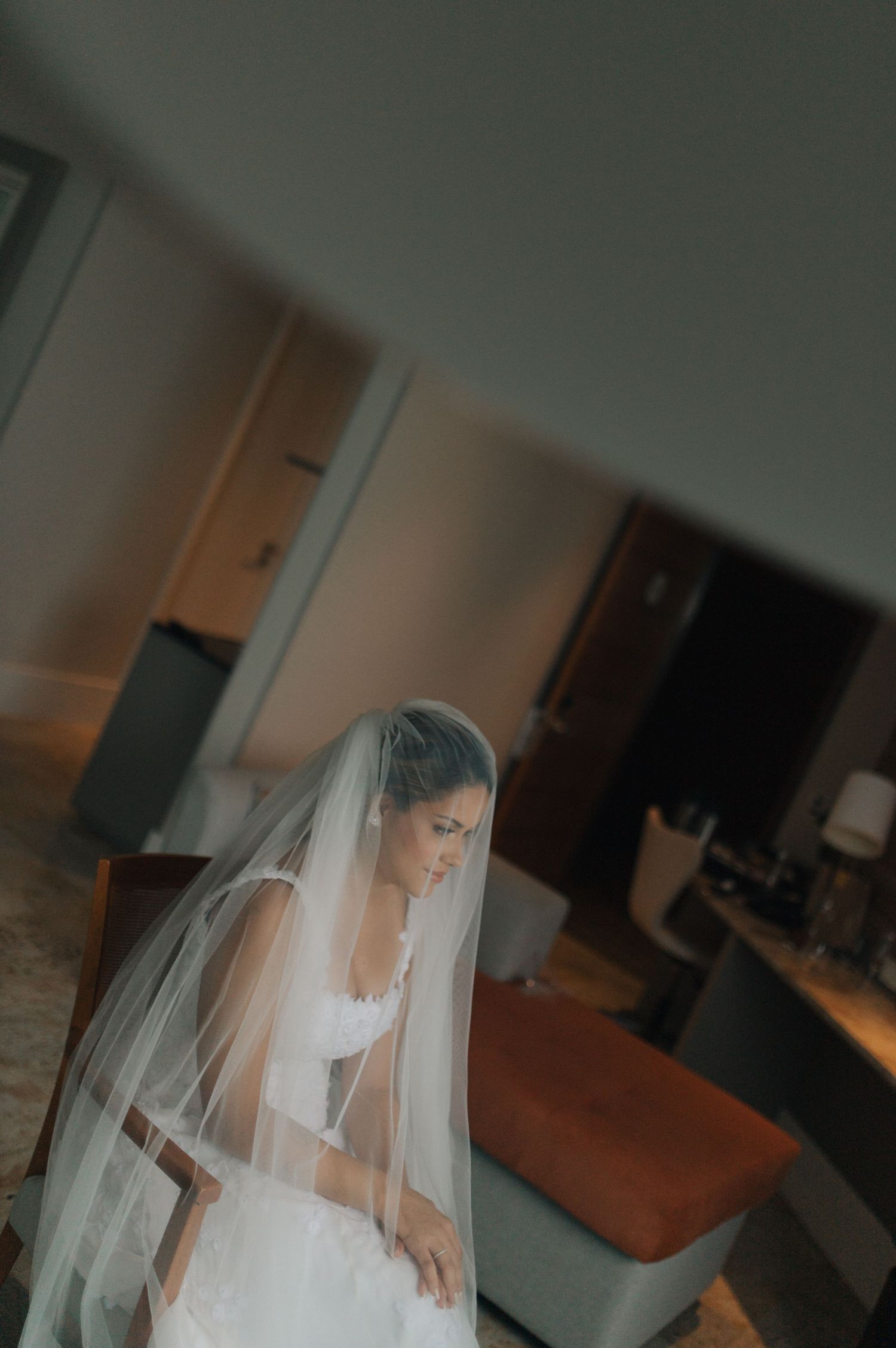 Candid shot of bride in white gown and long veil preparing in a hotel room.