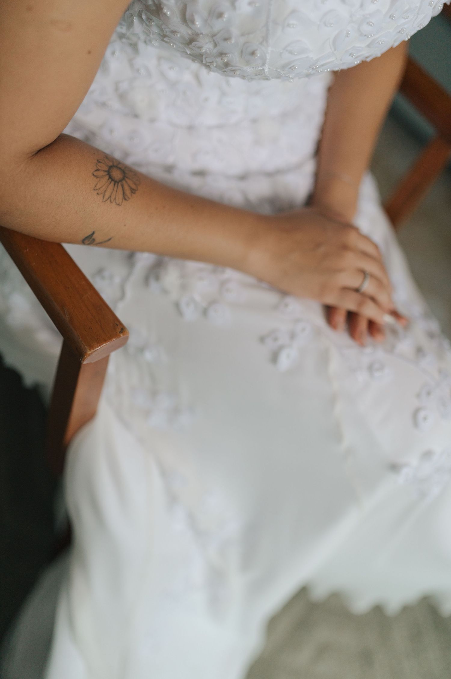 Detail shot of bride's hands resting on white lace dress with small tattoo visible.