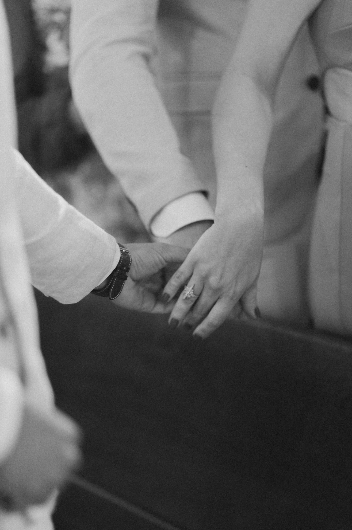 Black and white close-up of hands exchanging rings during wedding ceremony.