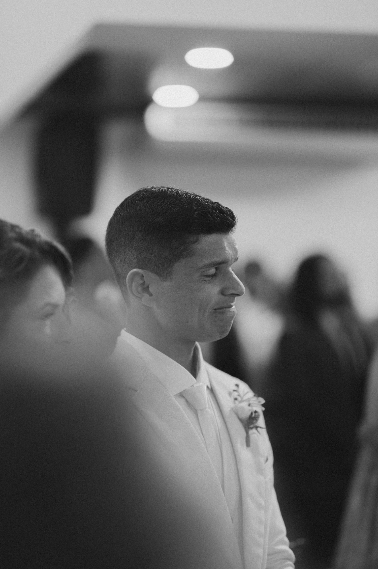 Black and white portrait of groom in white suit jacket smiling at wedding ceremony.