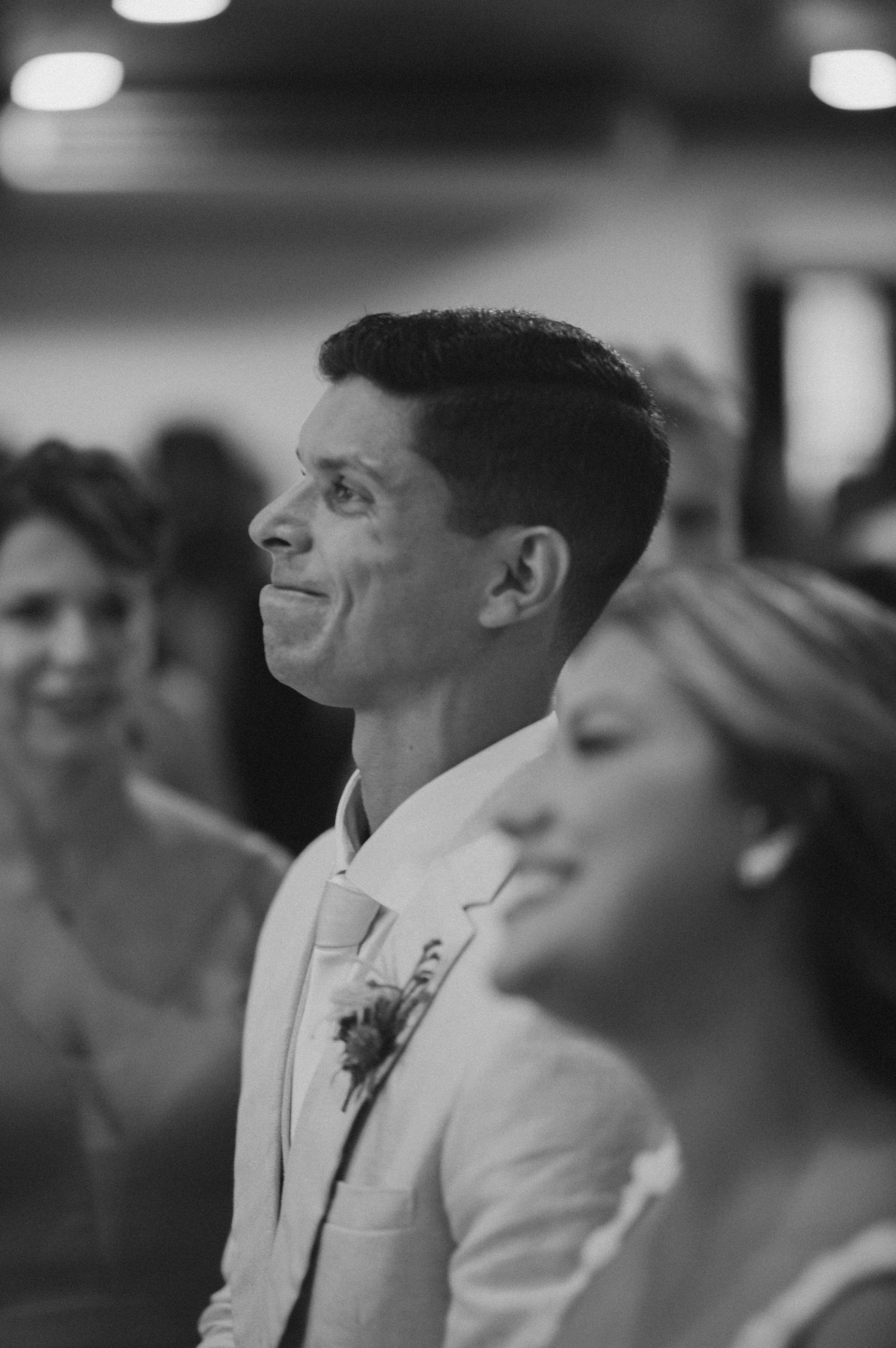 Black and white candid shot of groom smiling during wedding ceremony.