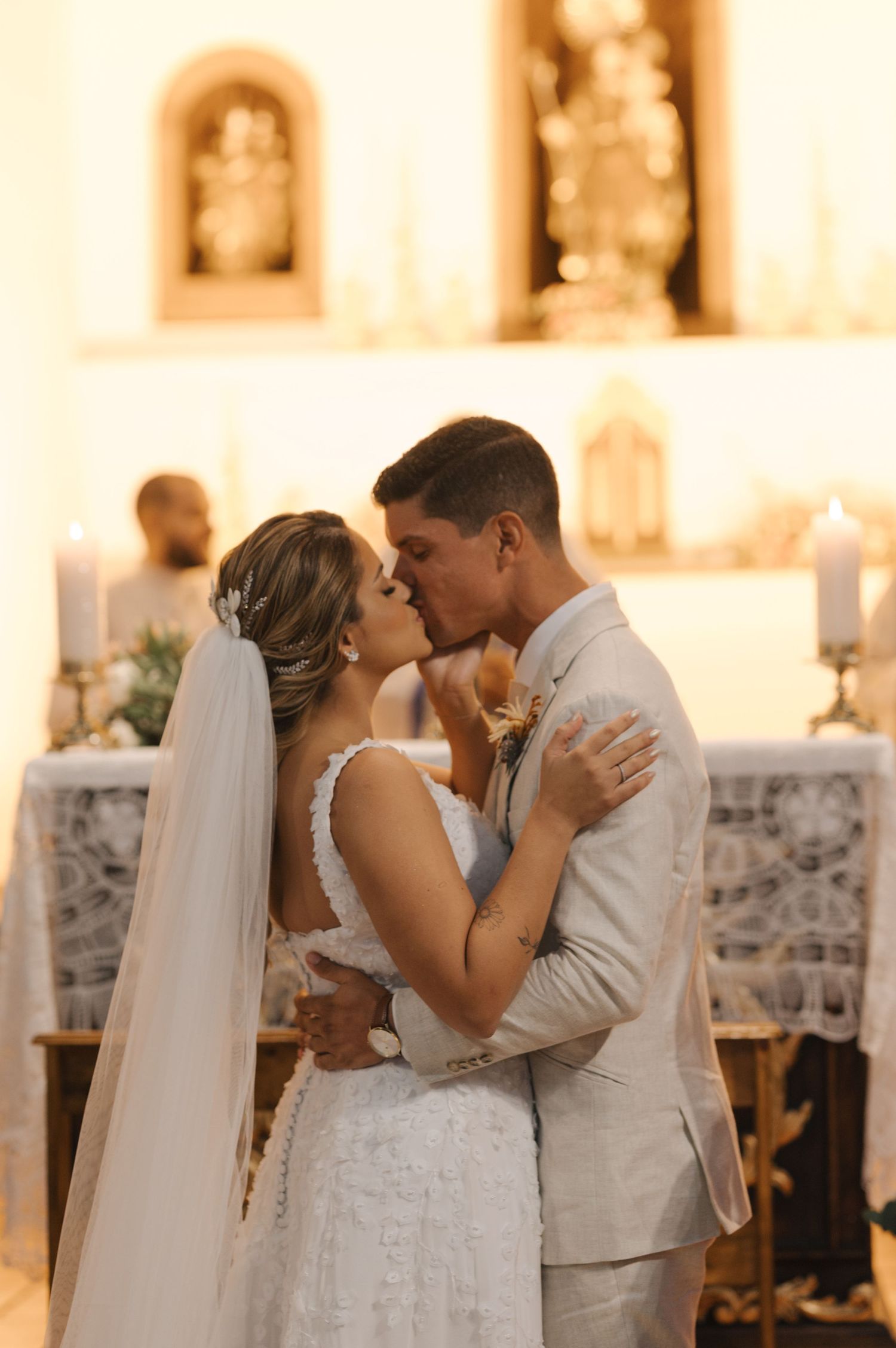 Bride and groom share first kiss at church altar with religious statues in background.