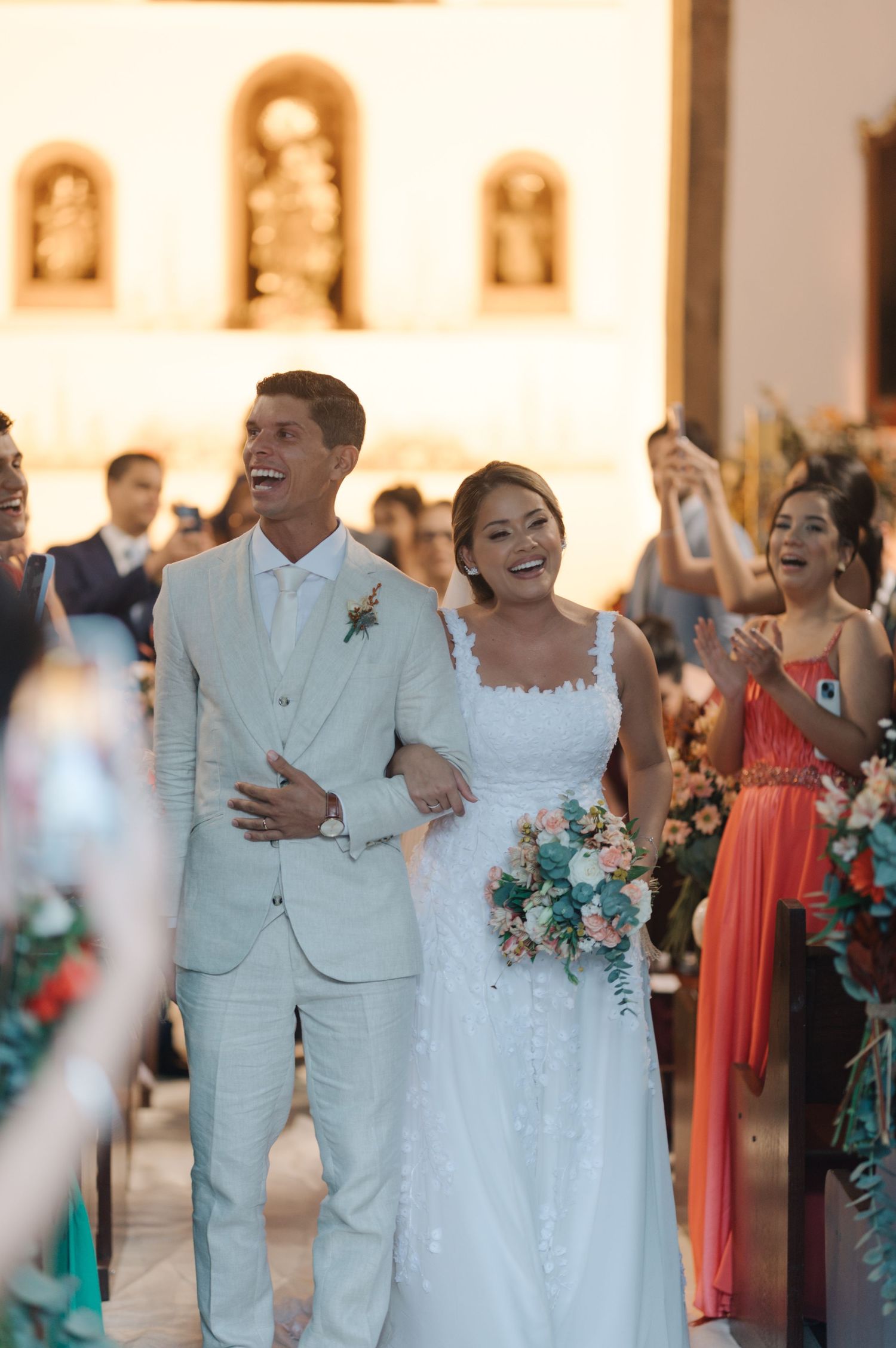 A joyous wedding couple walking down the aisle together in a sunlit church surrounded by guests.