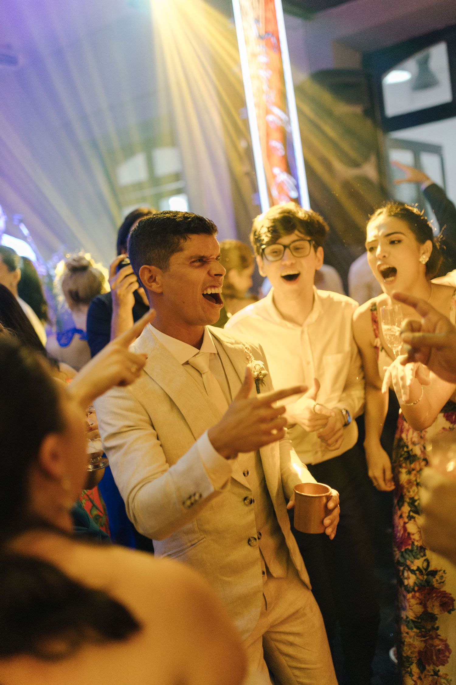Wedding guests dancing and singing enthusiastically at a lively reception party.
