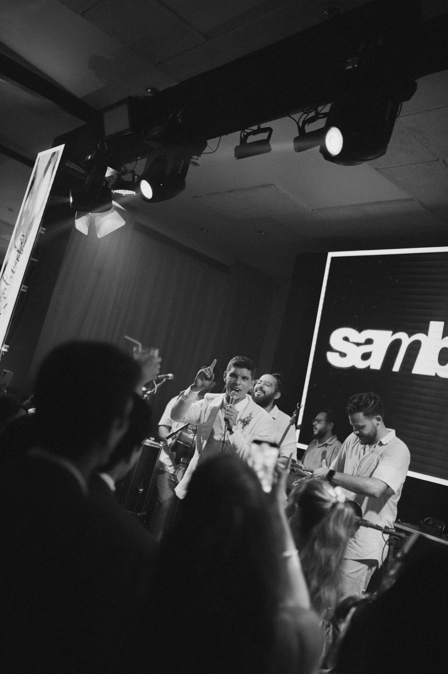 Musicians perform on stage with 'Samban' sign in background during nighttime concert venue performance.