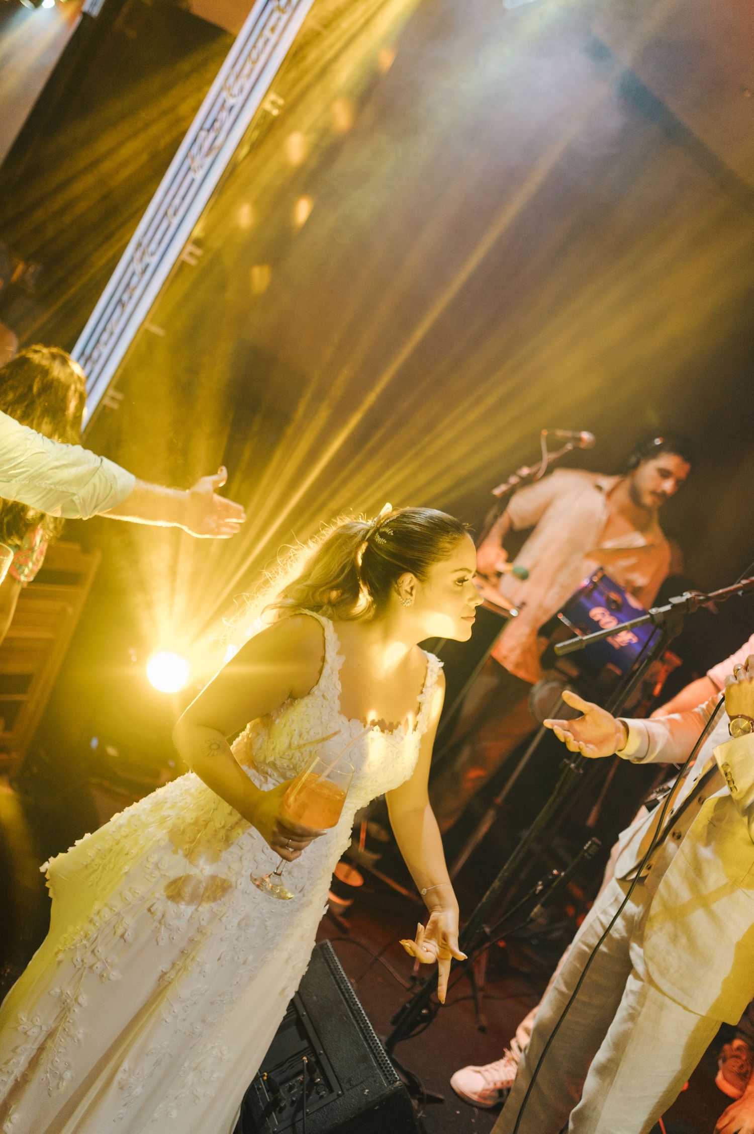 Performer in white dress illuminated by golden stage lights during energetic show.