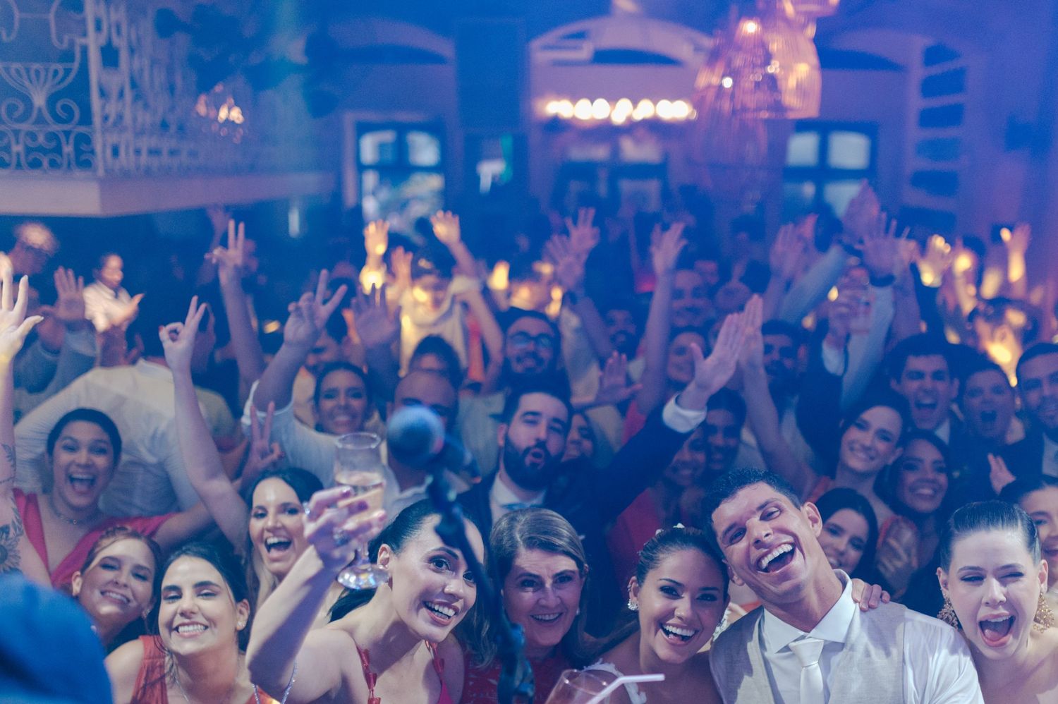 Enthusiastic crowd with raised hands enjoying performance in dimly lit venue with purple lighting.
