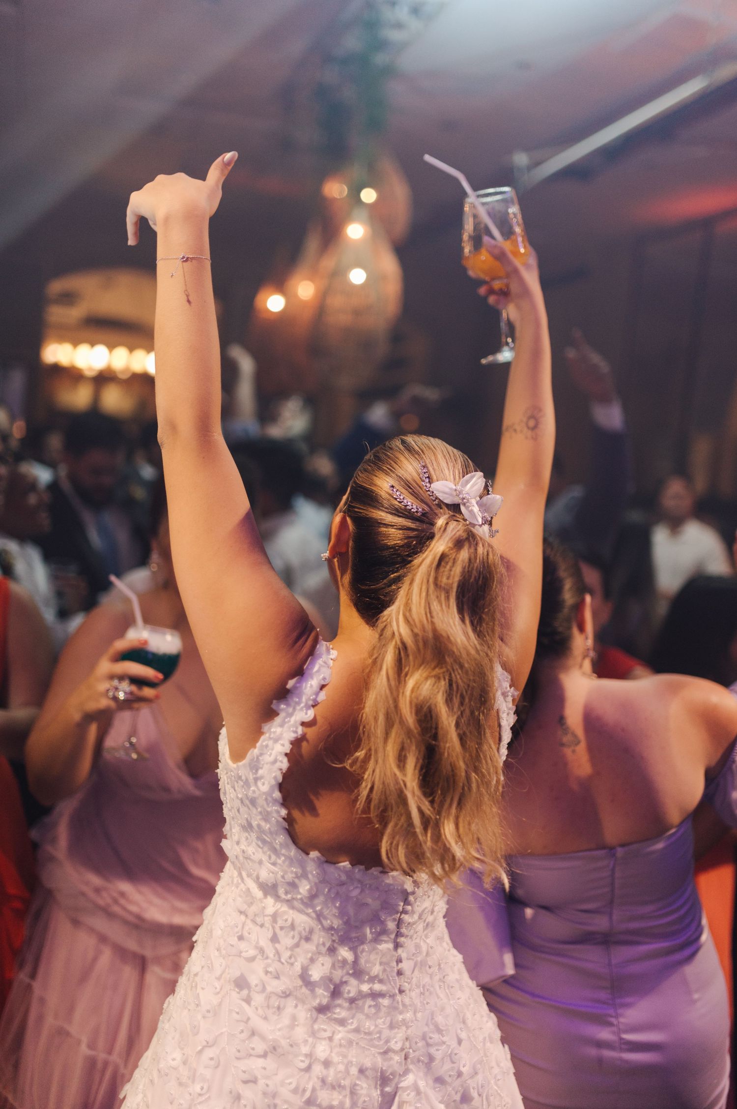 Person in white wedding dress raises arms while dancing at reception celebration.