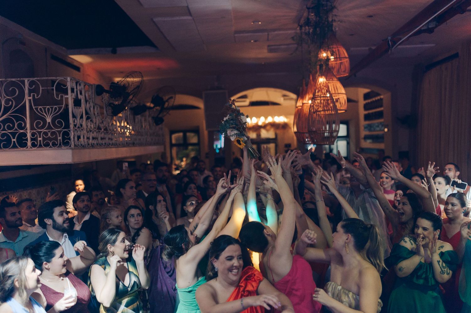 Crowd of party guests with raised arms dancing and celebrating in a dimly lit venue.