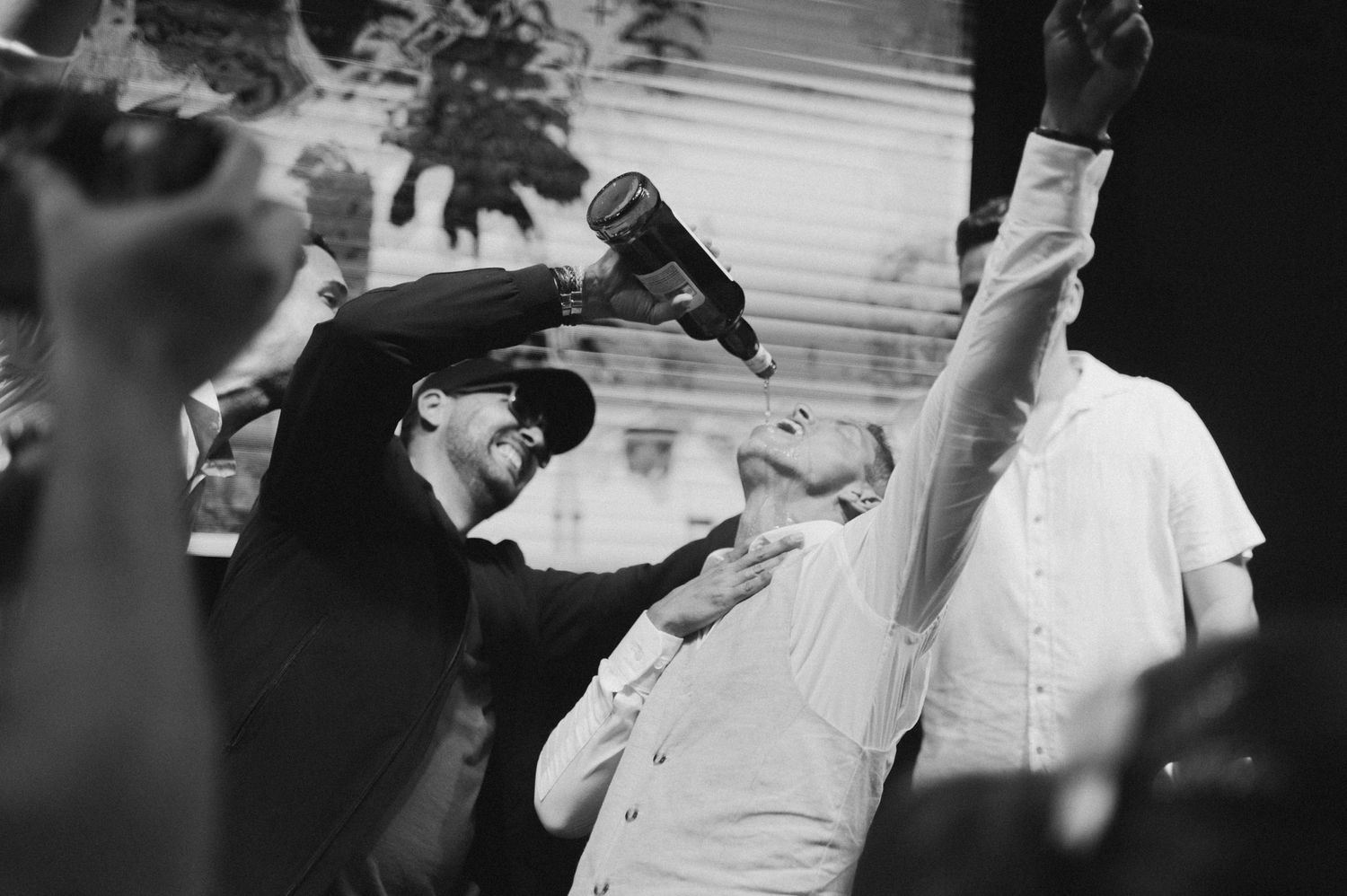 Black and white photo of people with raised bottles celebrating at a party.