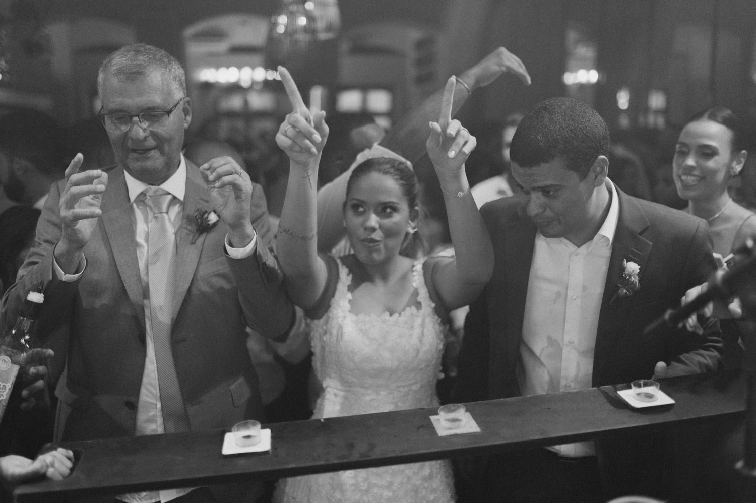 Wedding couple and guest celebrating at a bar counter in black and white photography.
