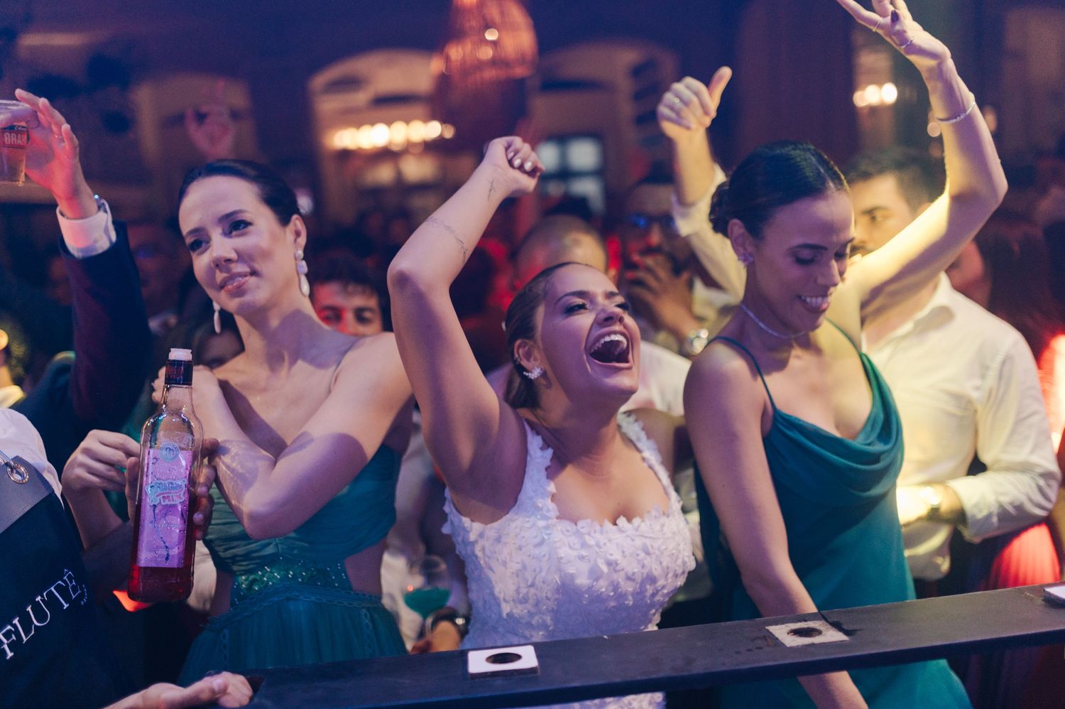 Wedding party celebrating with raised arms and drinks at a bar counter.