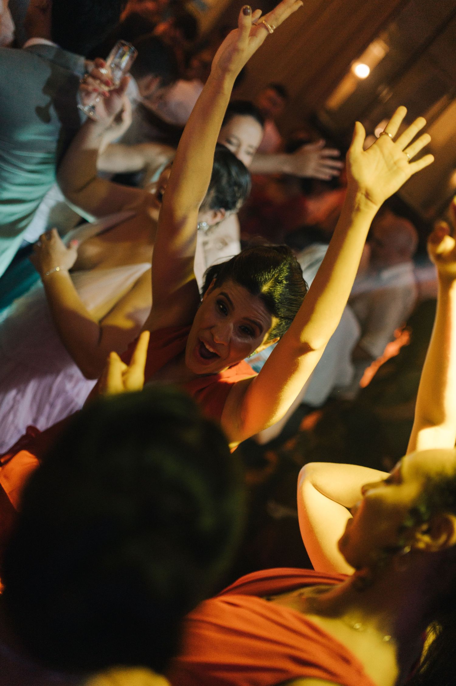 Enthusiastic party guests with raised arms dancing under warm lighting.