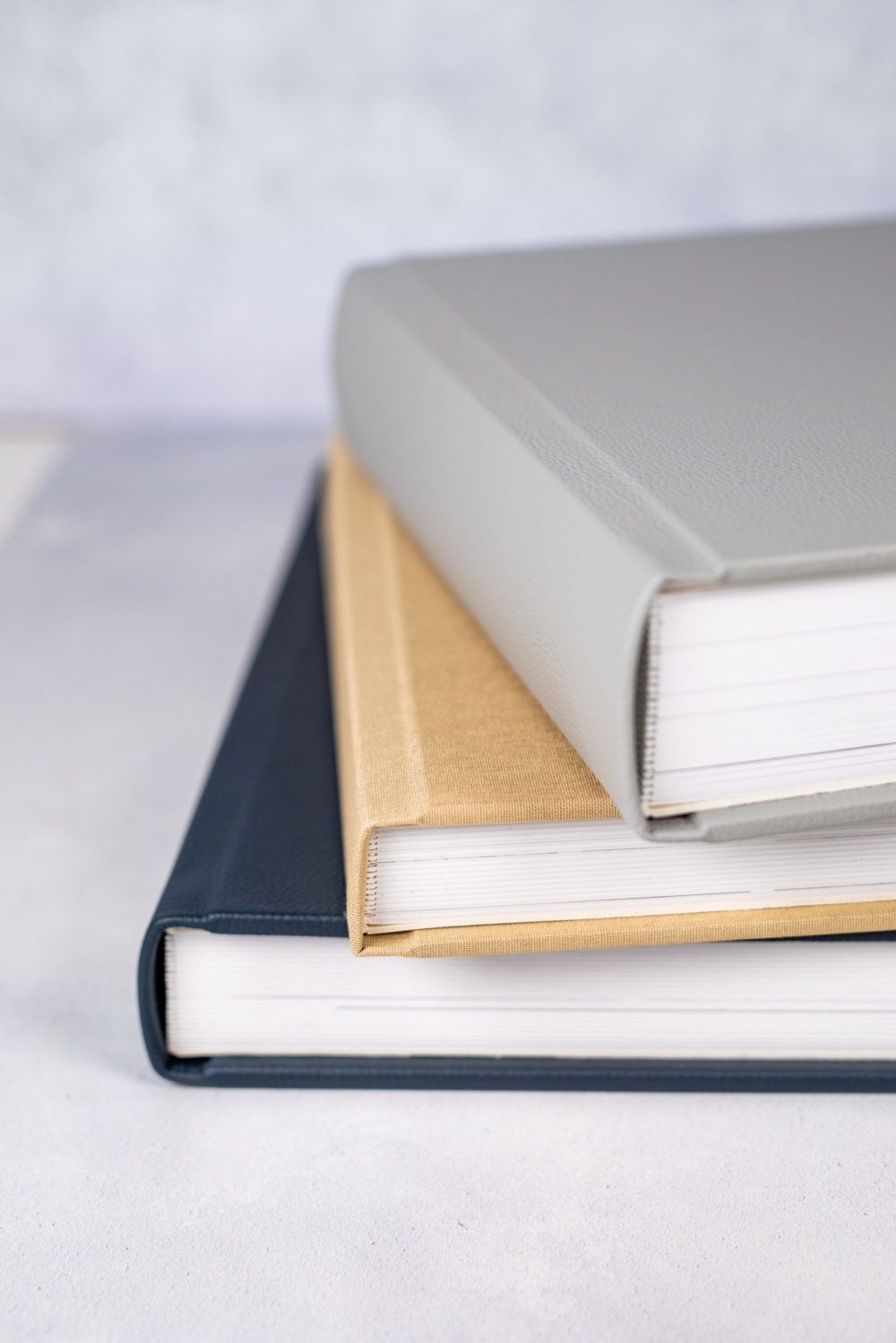 Stack of three hardcover books in navy, beige and gray colors arranged on a light surface with minimalist composition.