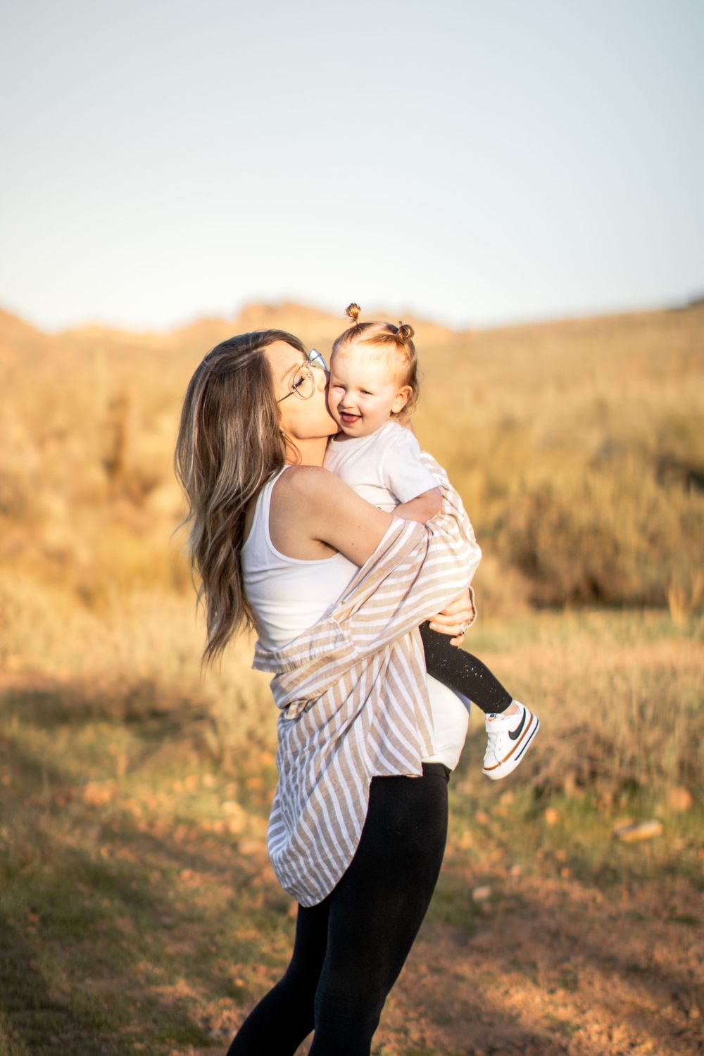 An expectant mother holds her toddler on her growing belly and gives her a kiss.The toddler is overjoyed.