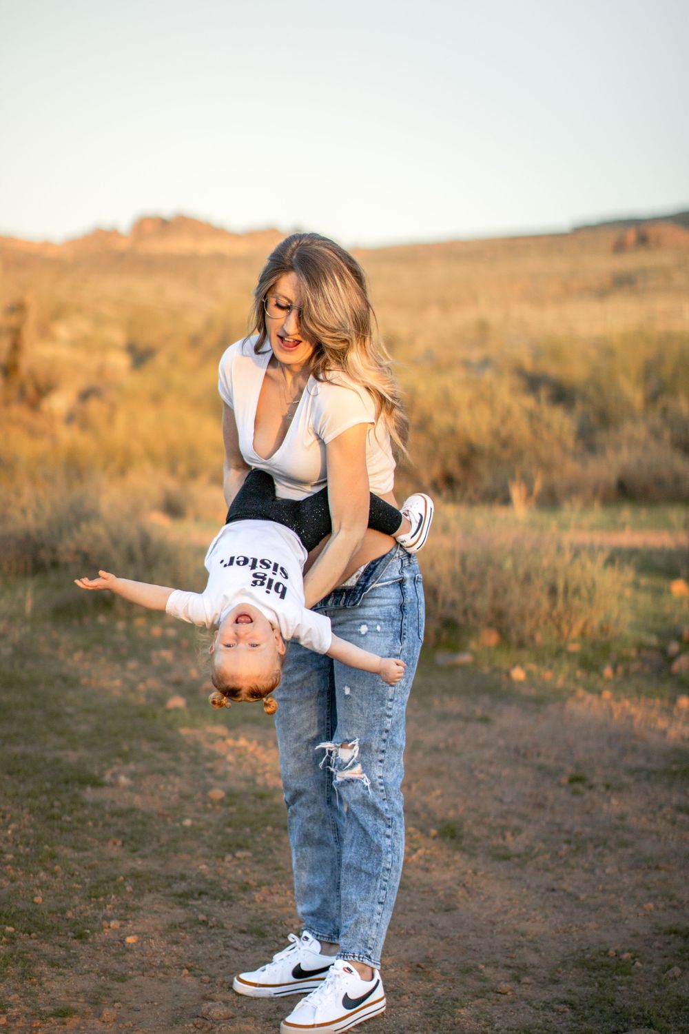 An expectant mother plays with her young daughter, holding her upside down. The toddler is beaming.
